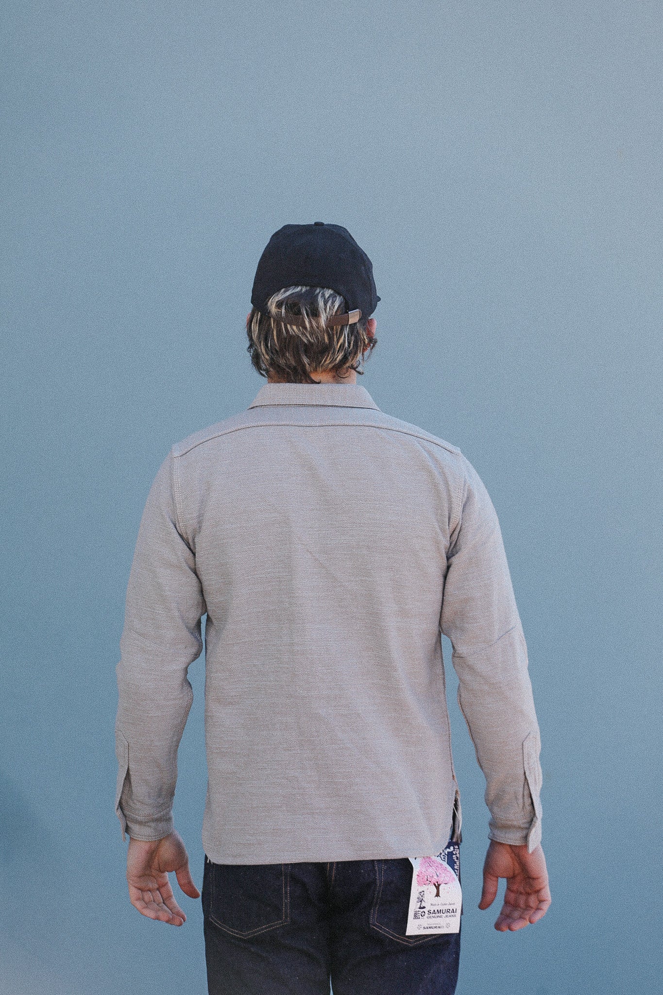 Person wearing a gray long-sleeve shirt and black cap with a blue background