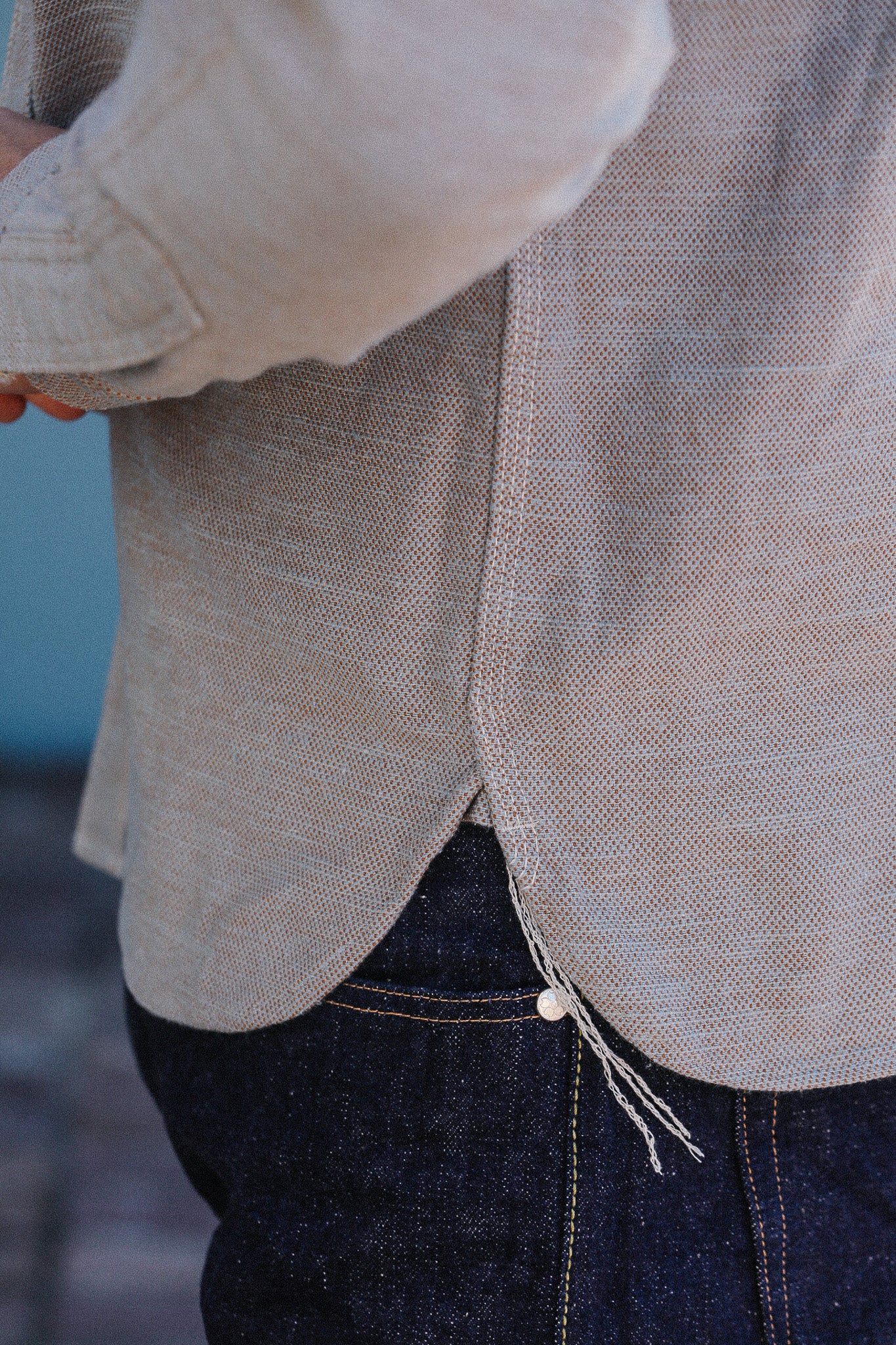 Close-up of a person wearing a beige jacket and dark jeans with a blurred background