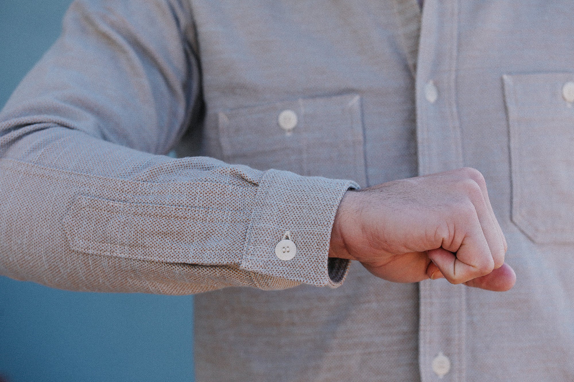 Person wearing a light gray button-up shirt with rolled-up sleeve against a blue background
