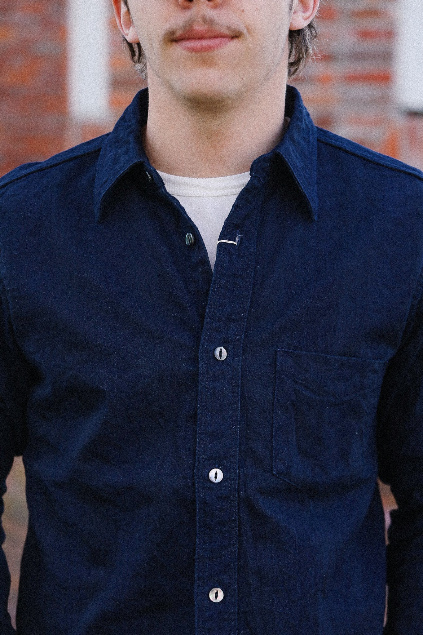 Man wearing a navy blue button-up shirt with a brick wall background