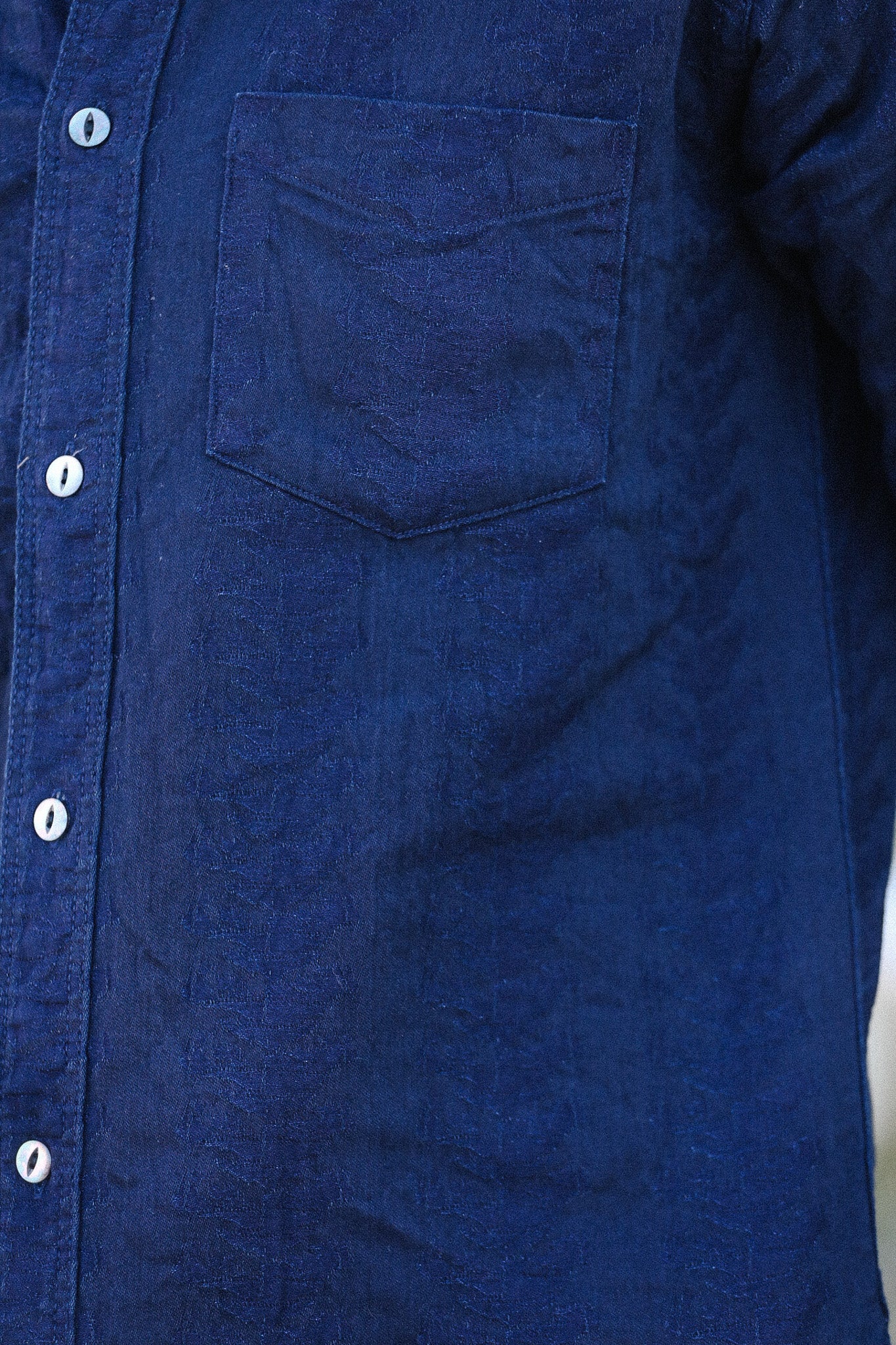 Close-up of a blue denim shirt with a pocket and buttons.
