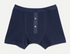 A pair of men's boxer briefs in dark navy blue, featuring a front button placket with two silver buttons, laid flat against a light off-white background.