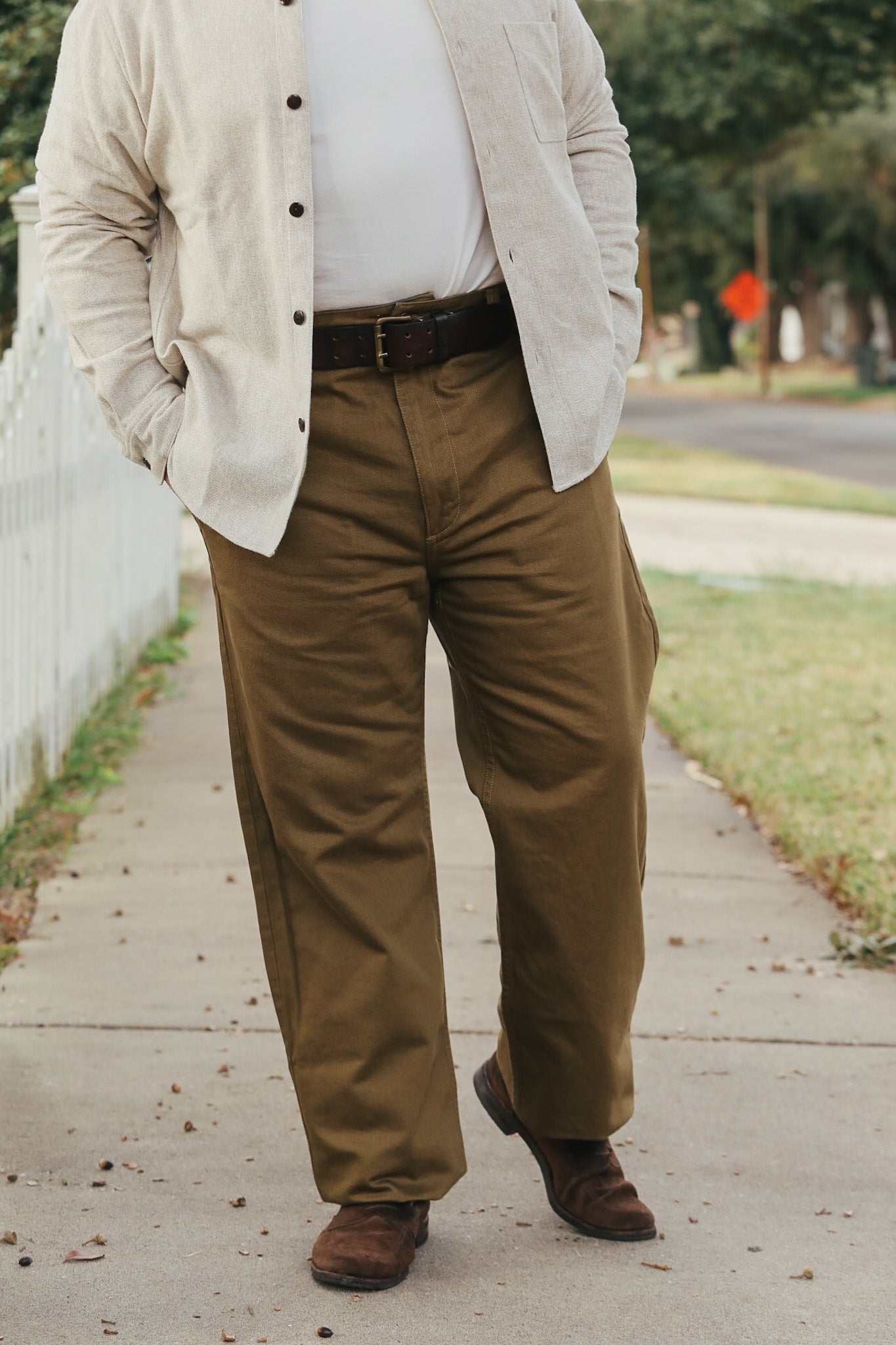 Person wearing a beige jacket, white shirt, and brown pants on a sidewalk.