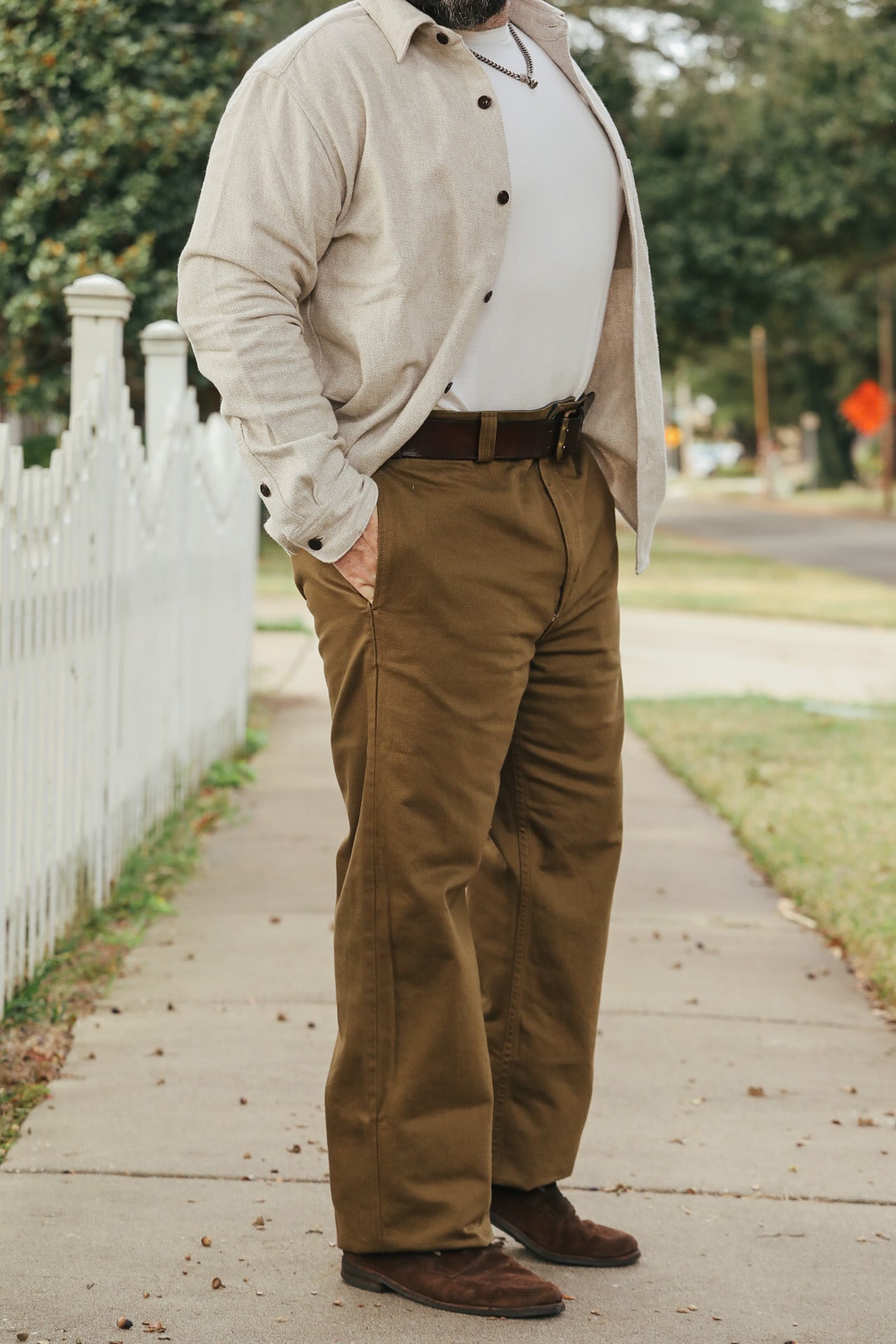 Man wearing a beige jacket, white shirt, and brown pants standing on a sidewalk.