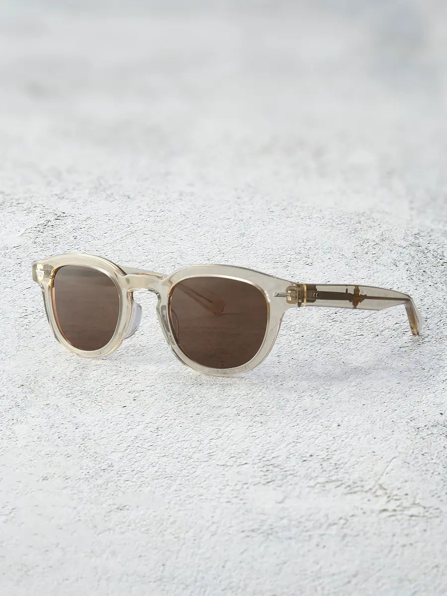 Sunglasses with a gold frame and brown lenses on a textured white surface