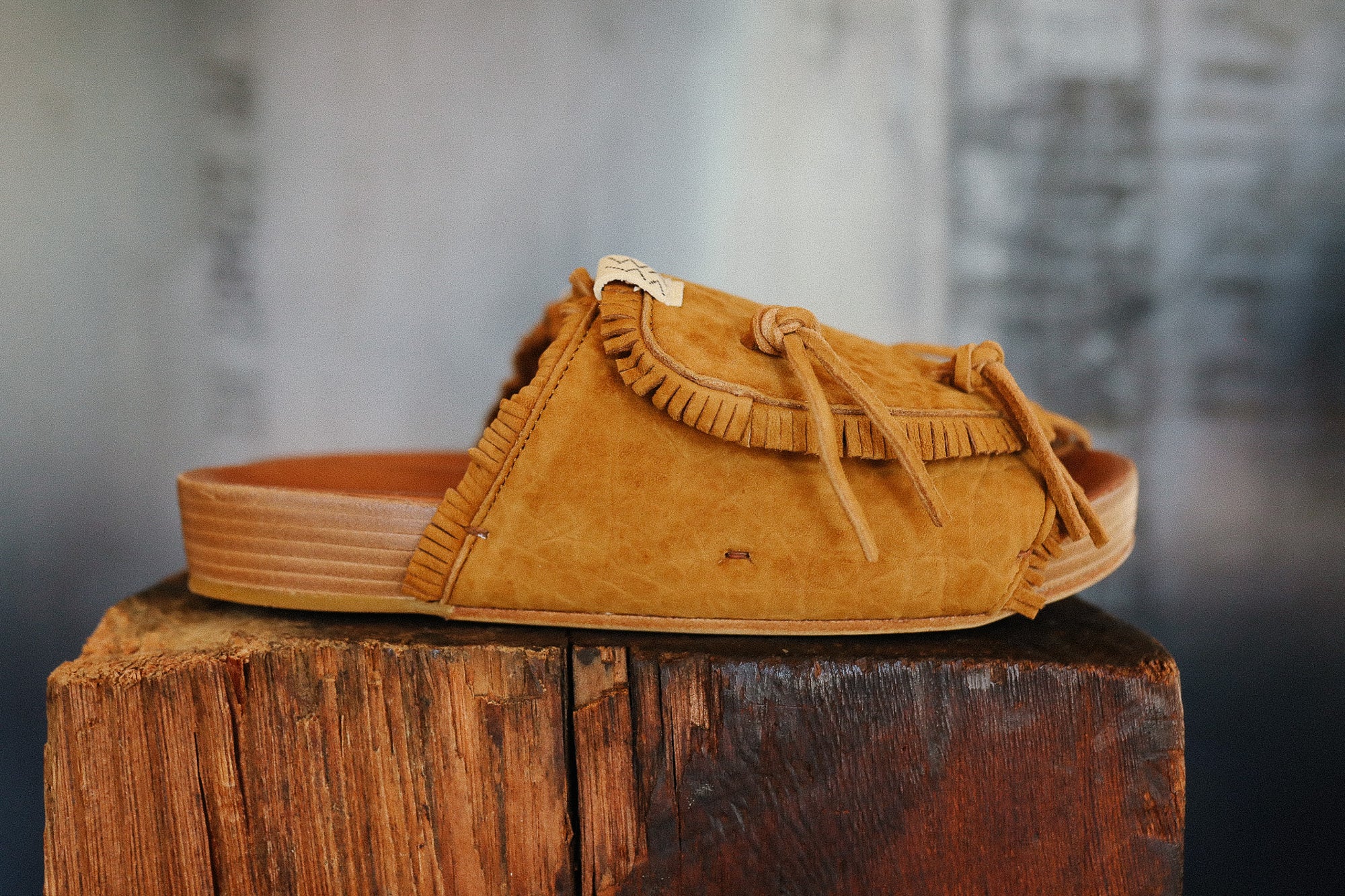 Brown suede sandal with fringes on a wooden block against a blurred background