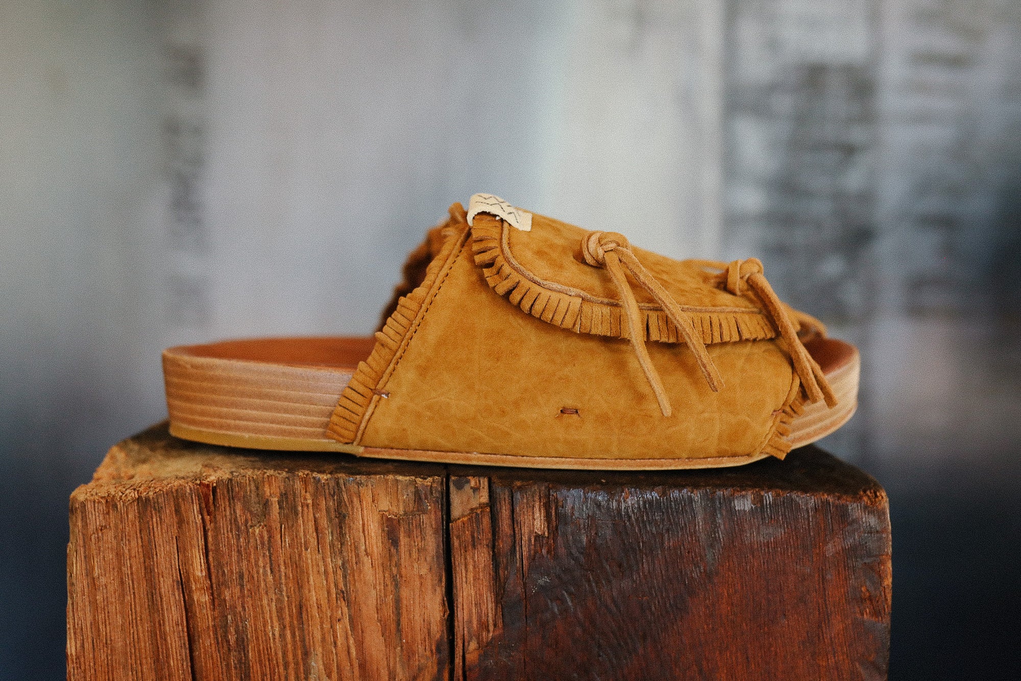 Brown suede sandal with fringes on a wooden block against a blurred background