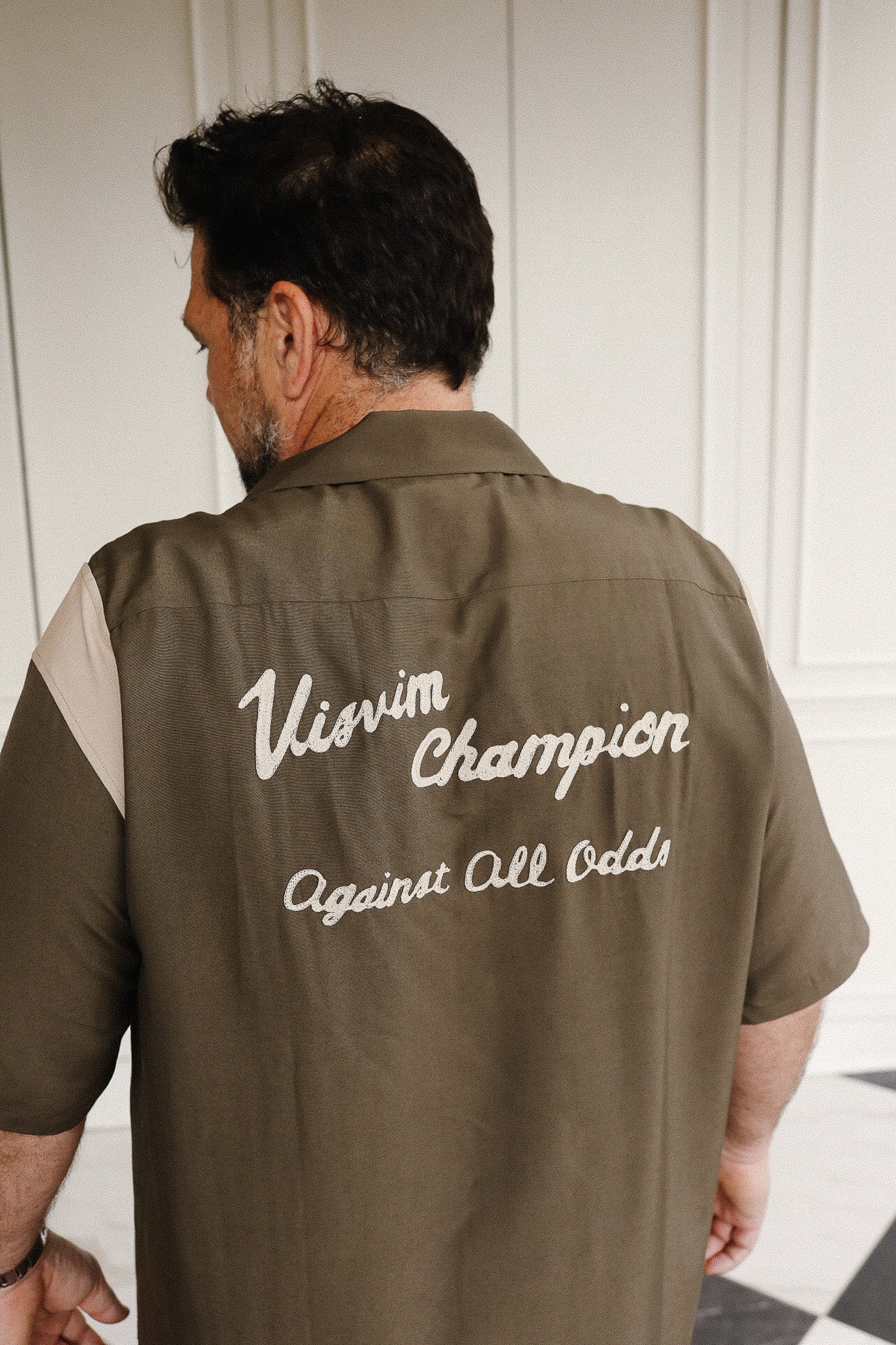 Man wearing a brown shirt with 'Vivian Champion Against All Odds' text.