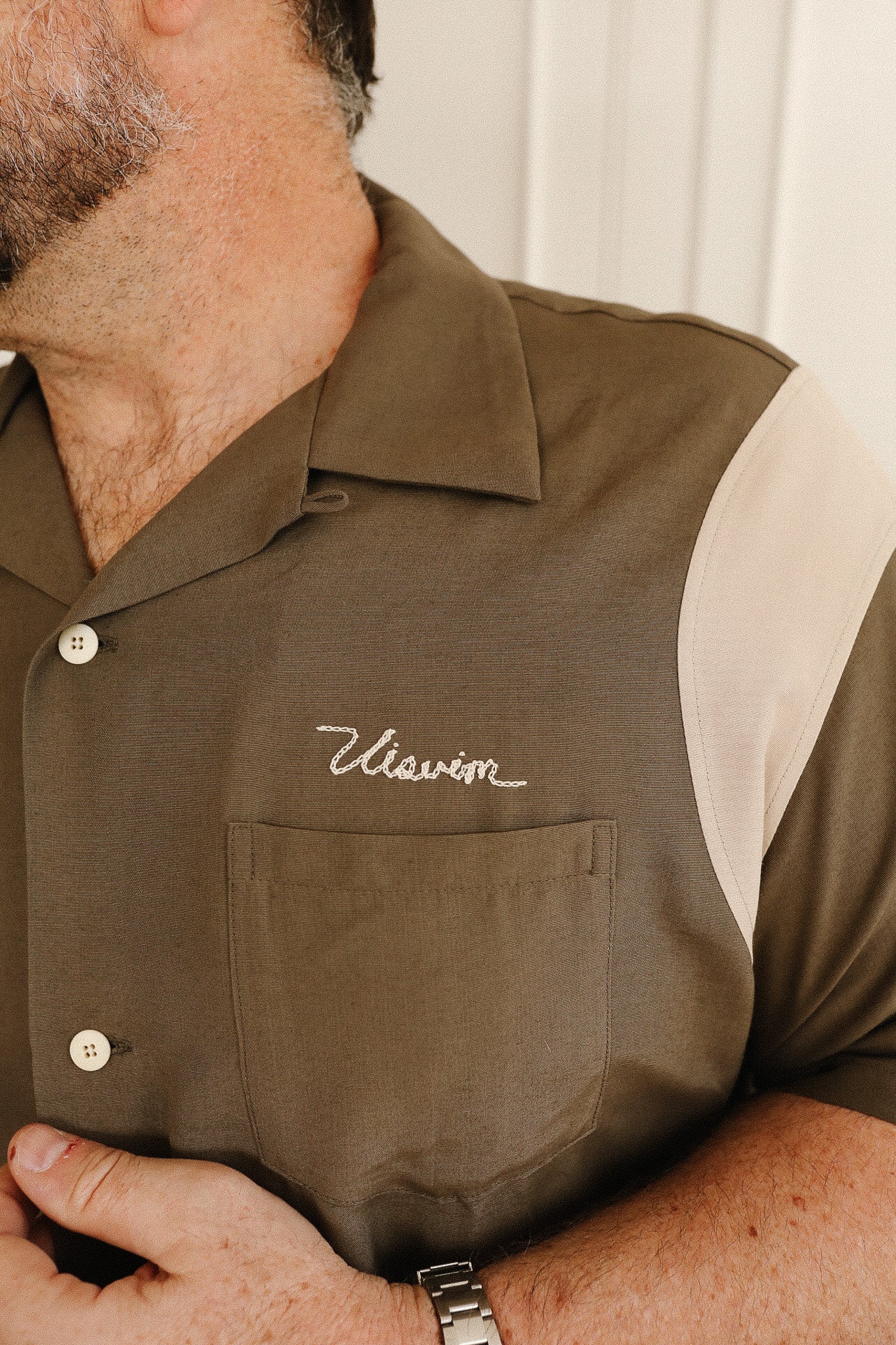 Close-up of a man wearing a brown shirt with a visible brand logo.