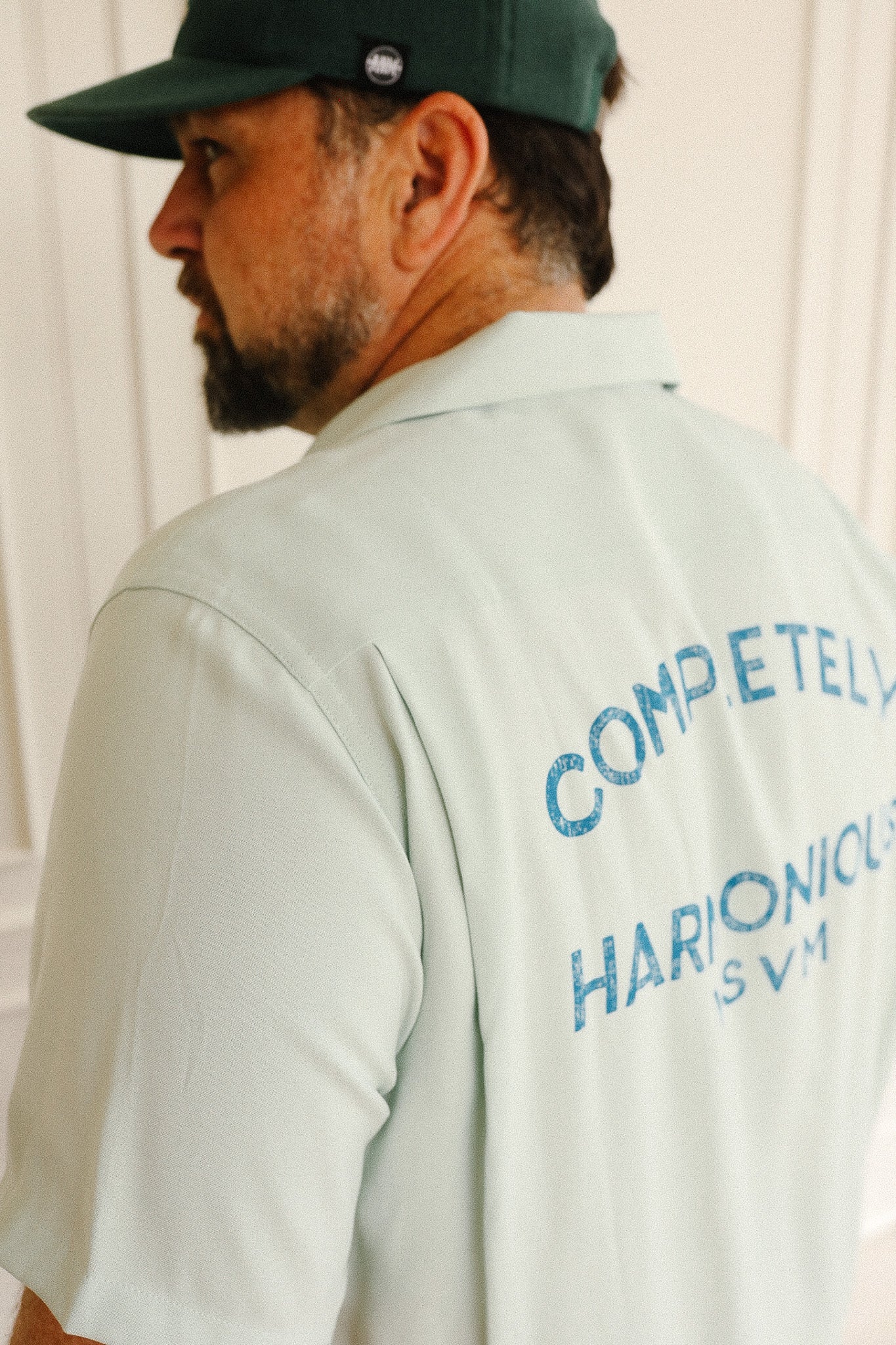 Man wearing a light-colored shirt with blue text on the back, standing against a plain background.