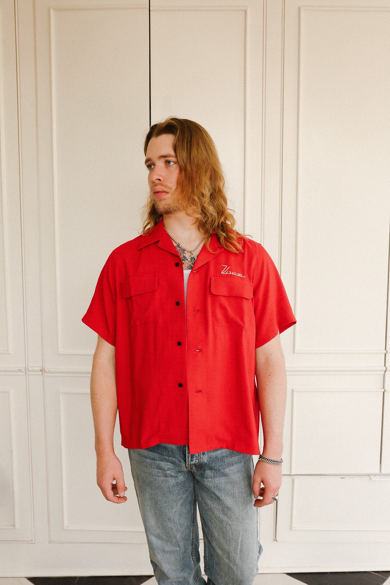 Person wearing a red shirt with a brand logo against a white paneled wall.