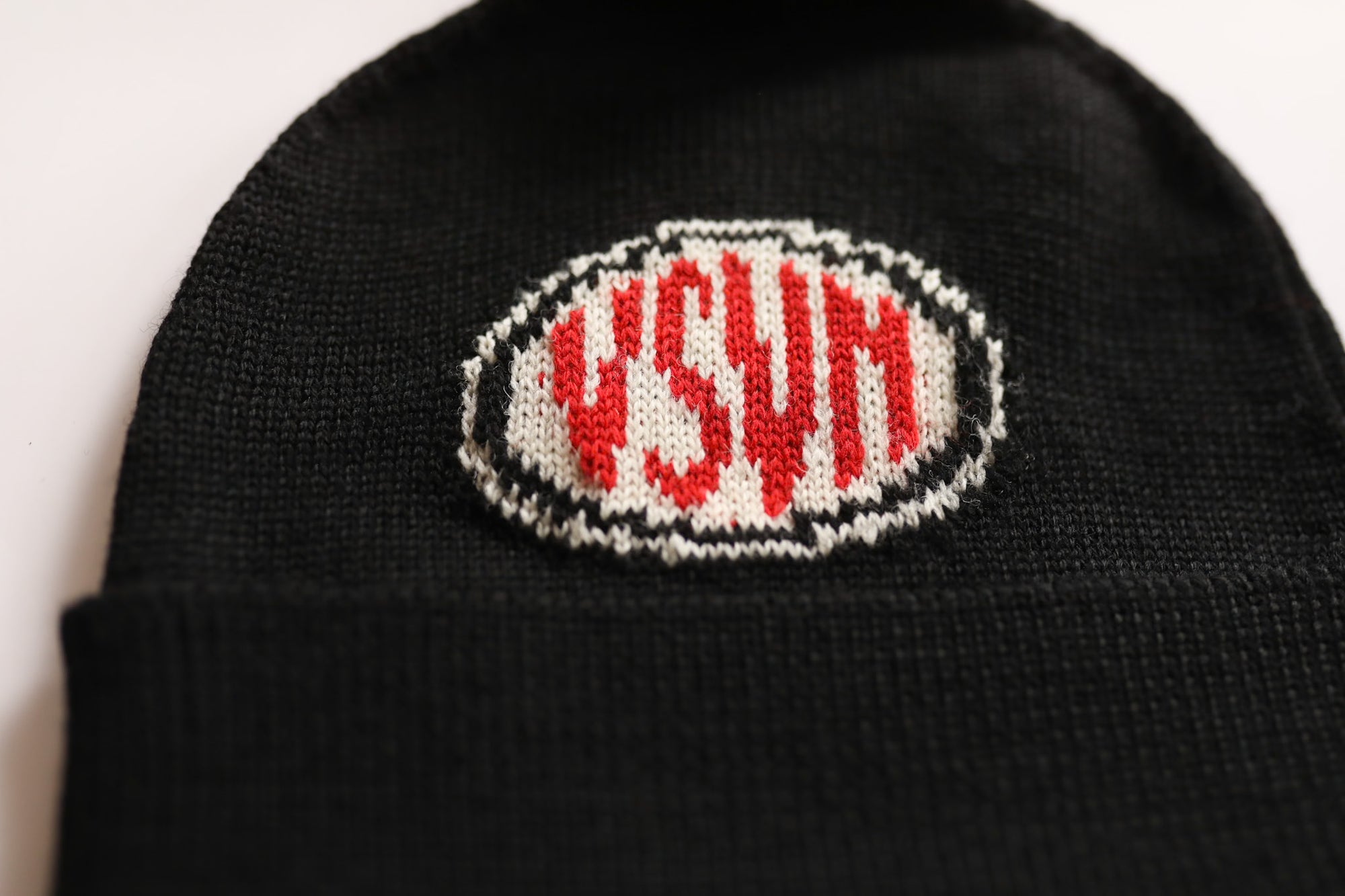Black beanie with a red and white logo on a light background