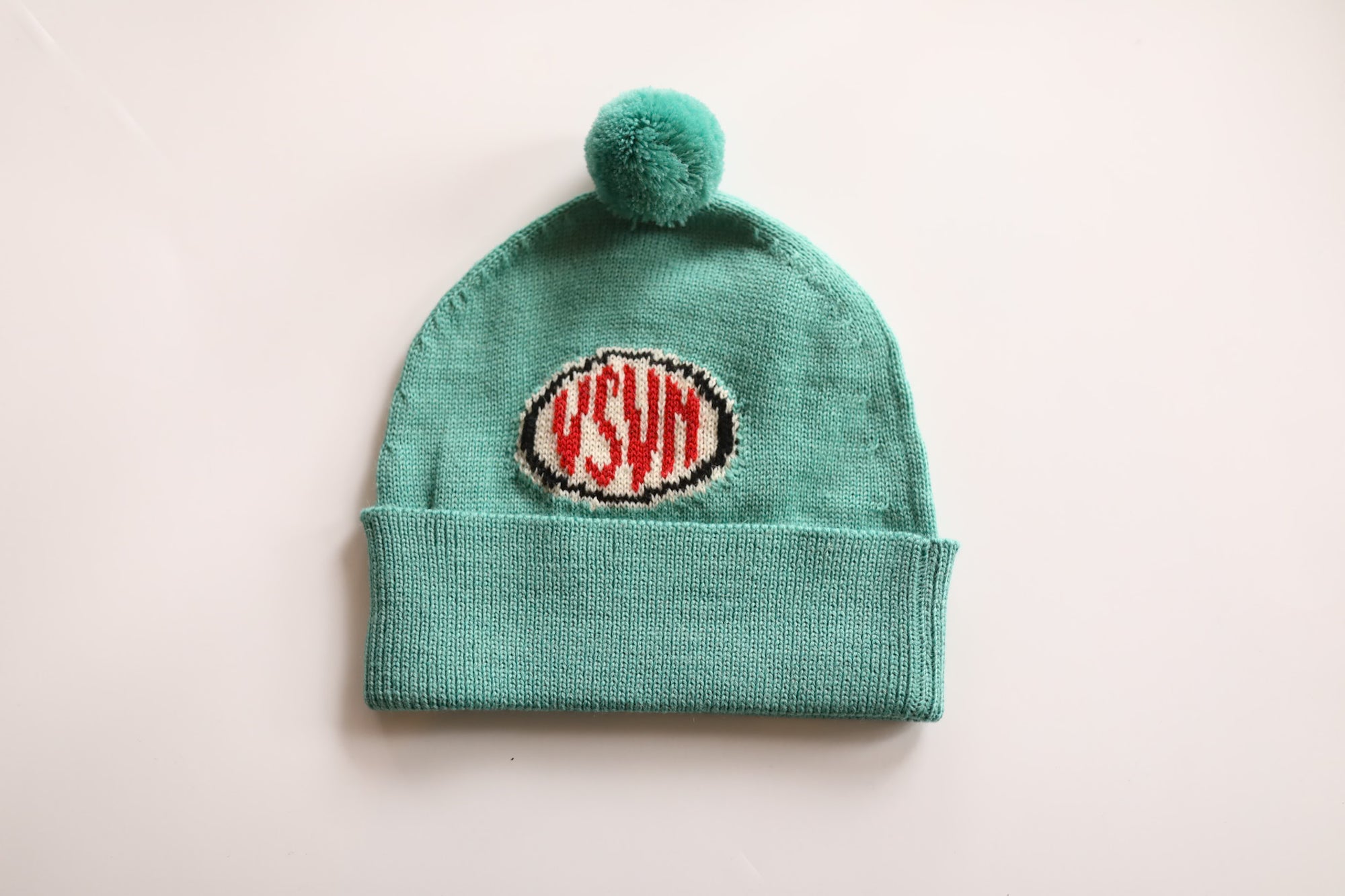 Green knit beanie with pom-pom on a light beige background