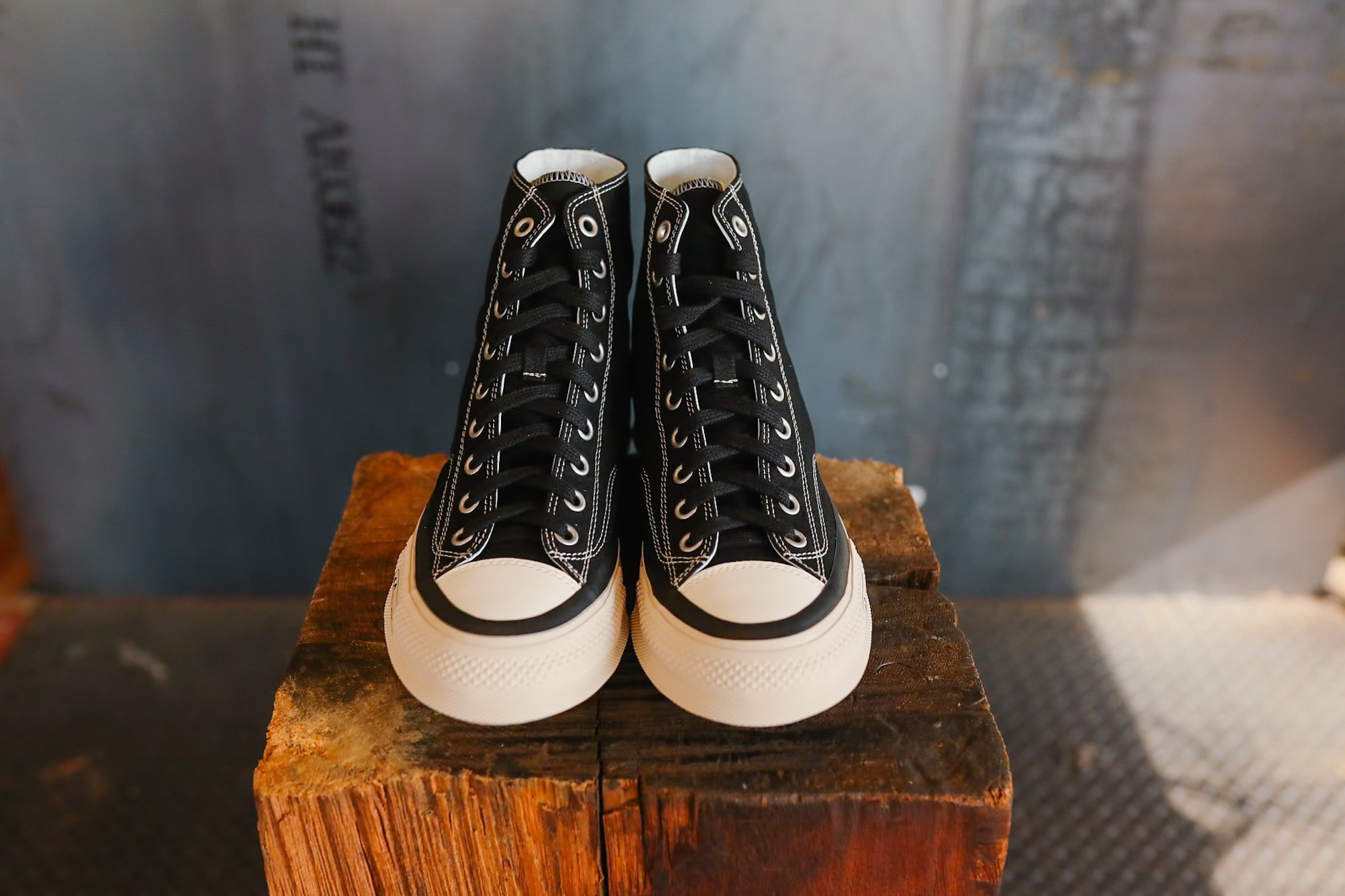 Pair of black high-top sneakers with white soles on a wooden block against a textured background
