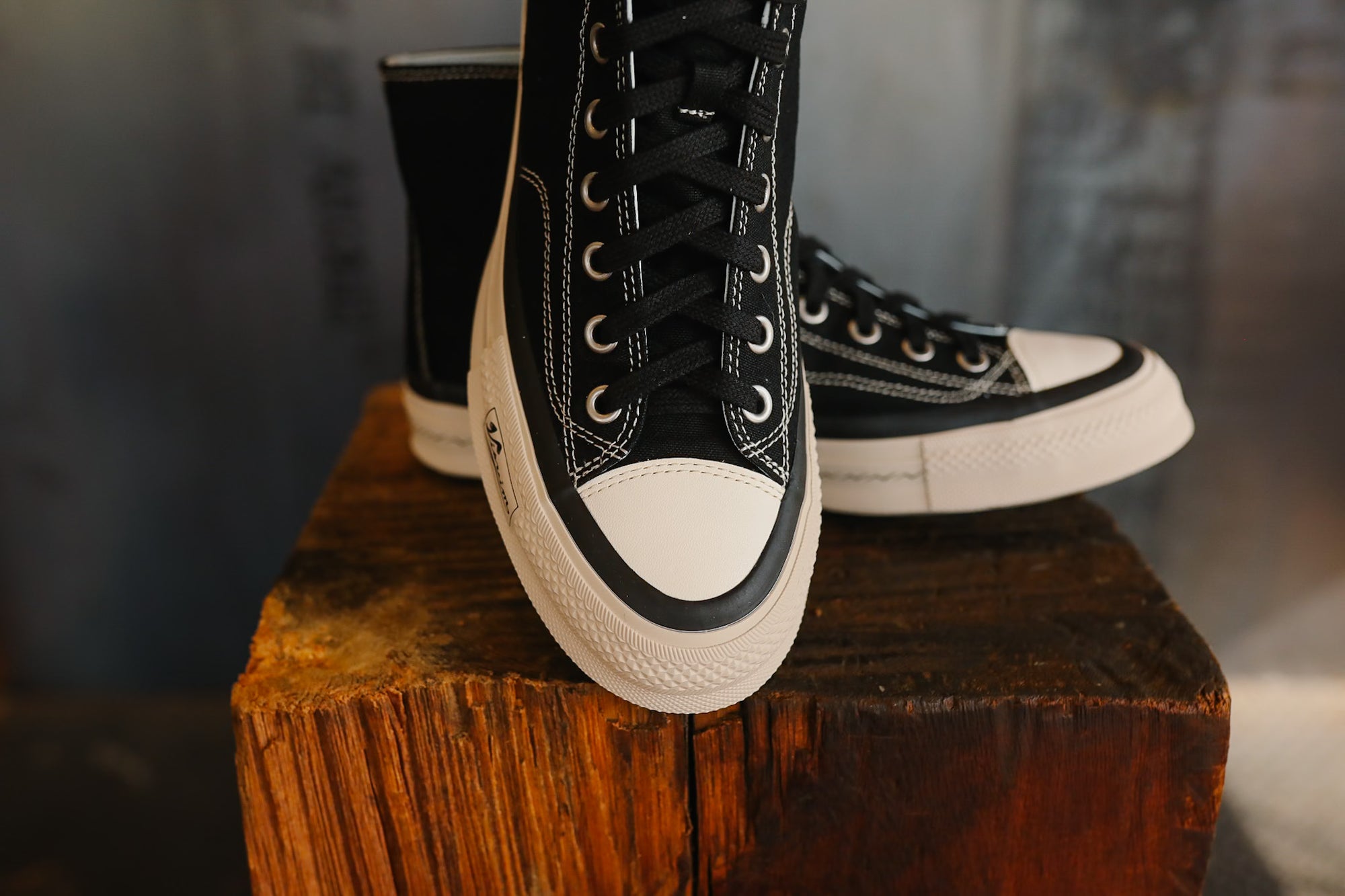Black high-top sneakers with white soles on a wooden block against a blurred background
