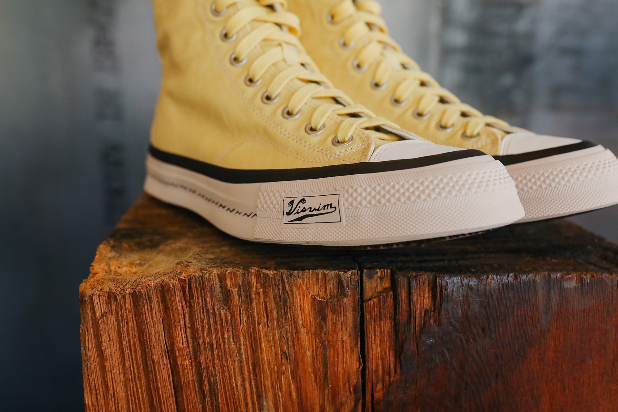 Yellow high-top sneakers with a visible brand logo on a wooden block.