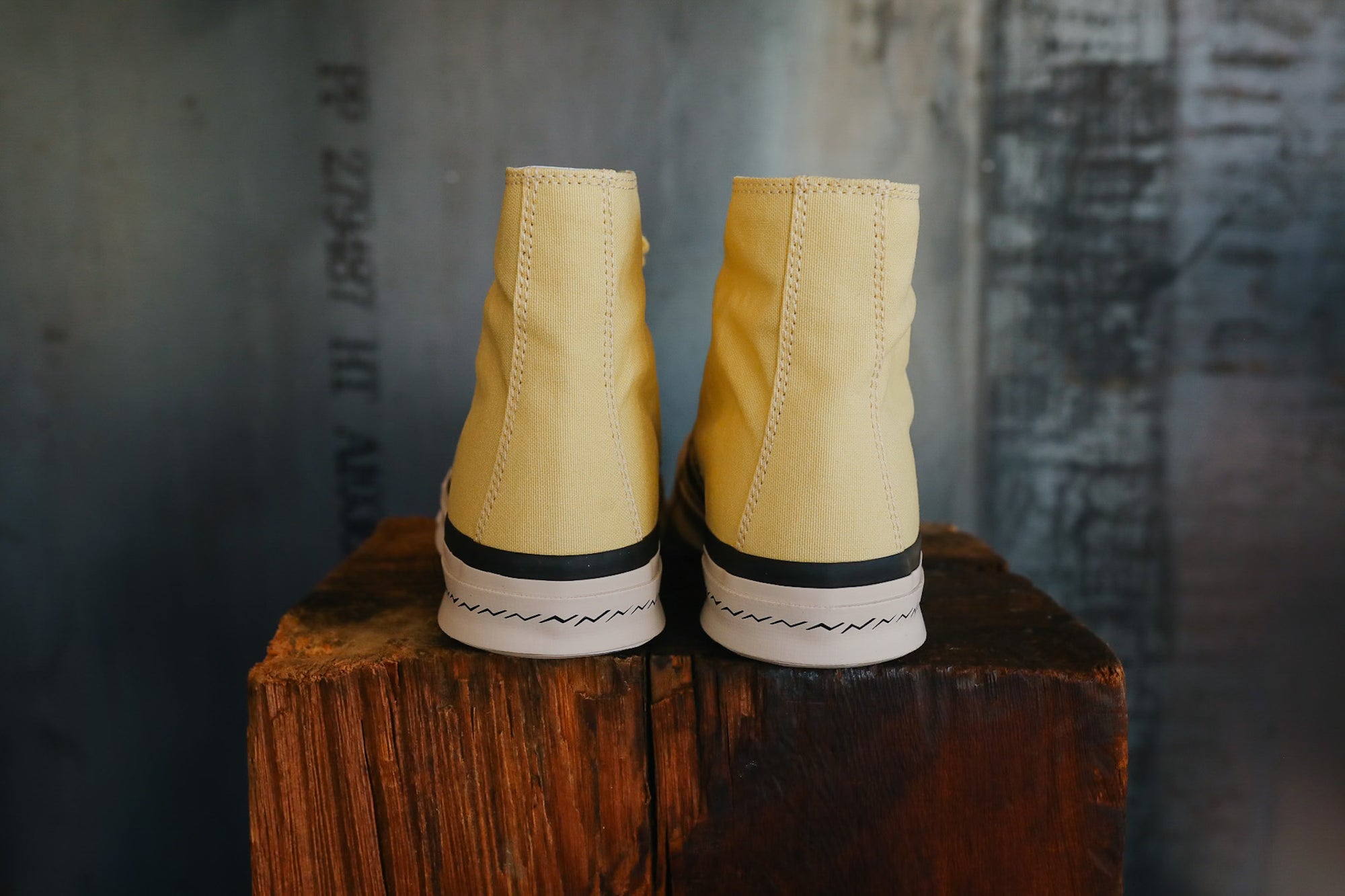 Pair of yellow high-top sneakers on a wooden block with a textured gray background