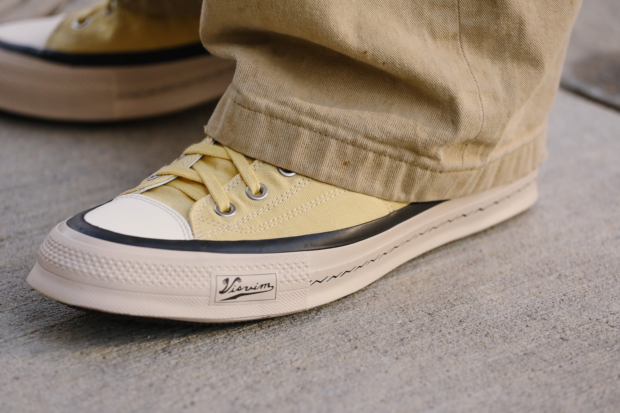 Close-up of a beige sneaker with black accents on a concrete surface
