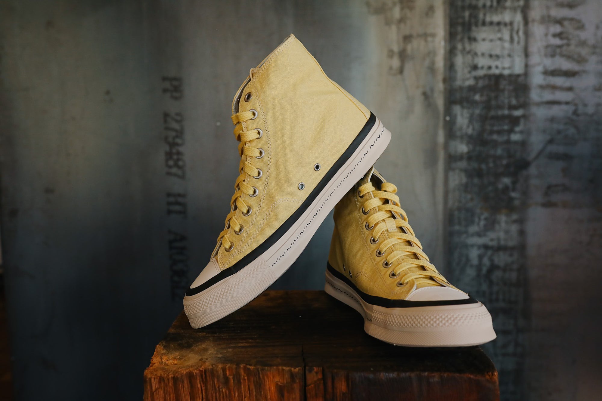 Yellow high-top sneakers with black accents on a wooden block against a textured wall.