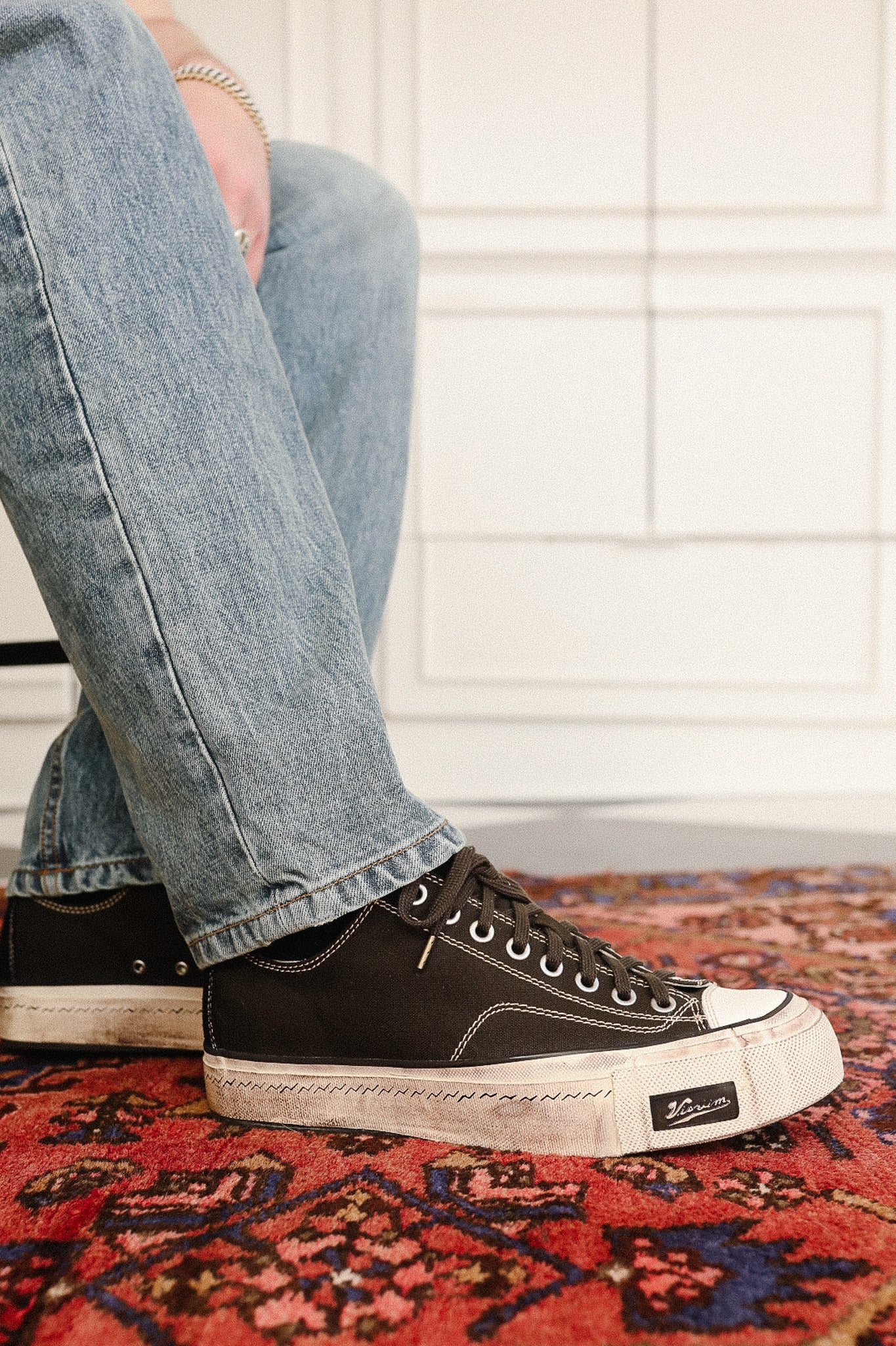 Person wearing black high-top sneakers with white soles on a red patterned rug.
