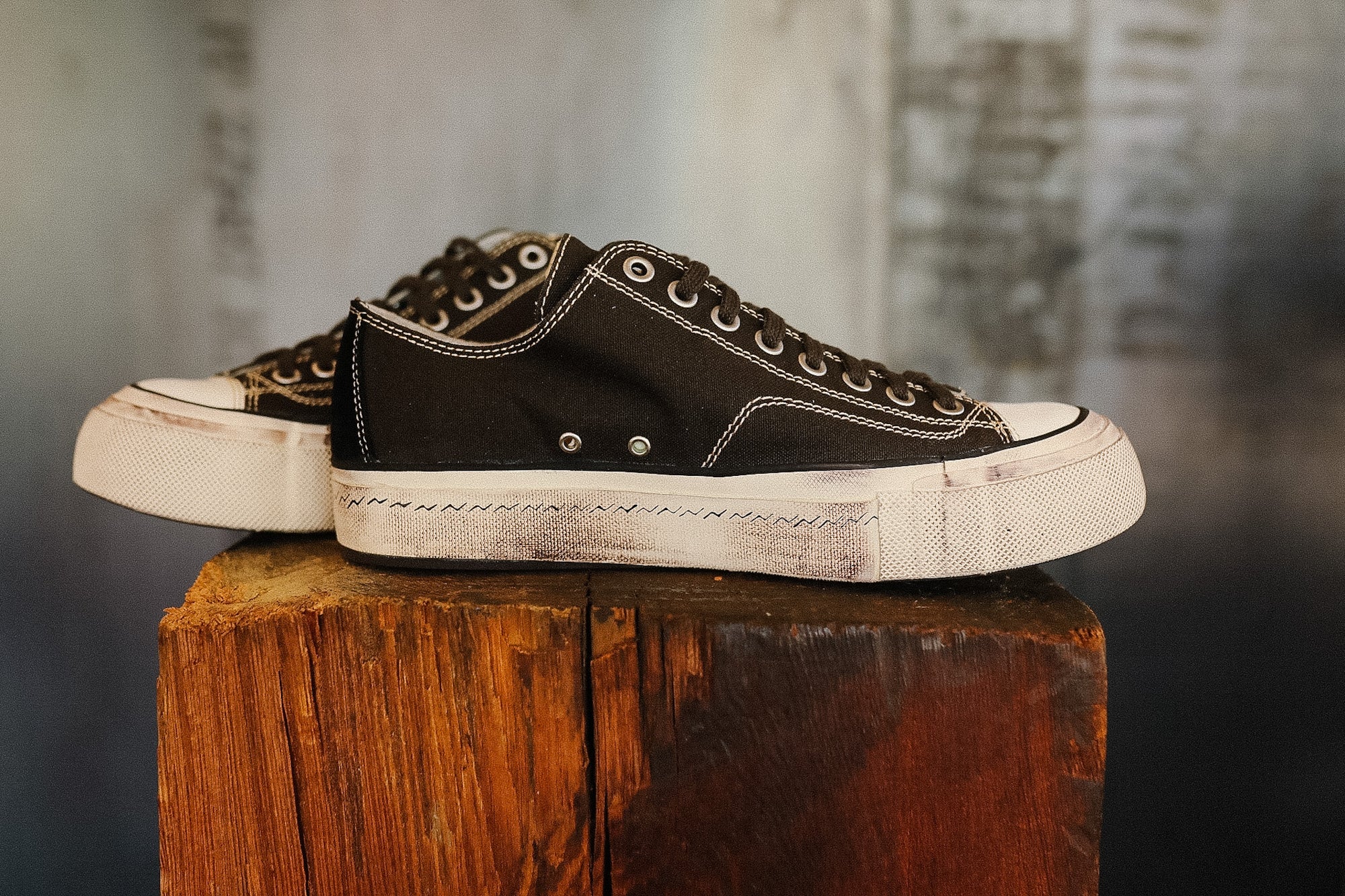 Pair of black sneakers with white soles on a wooden block against a blurred background