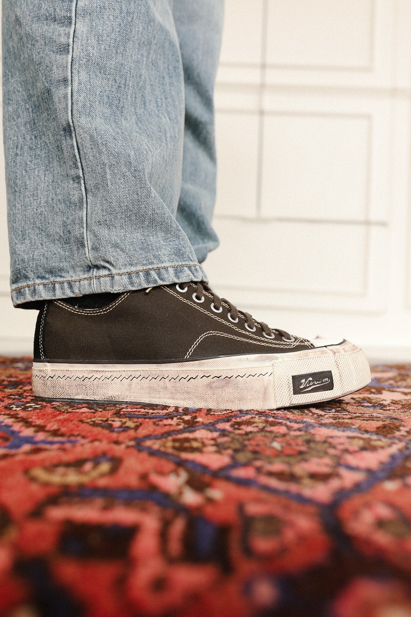 Person wearing black high-top sneakers with a brand logo on a patterned rug.