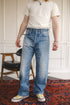 Person wearing light blue jeans and a white shirt standing on a patterned rug.