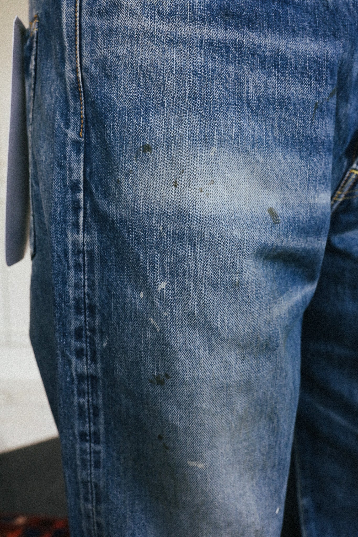 Close-up of a pair of blue denim jeans with visible dirt, stains, and scuffs on the thigh, showing the raw denim texture and stitching.