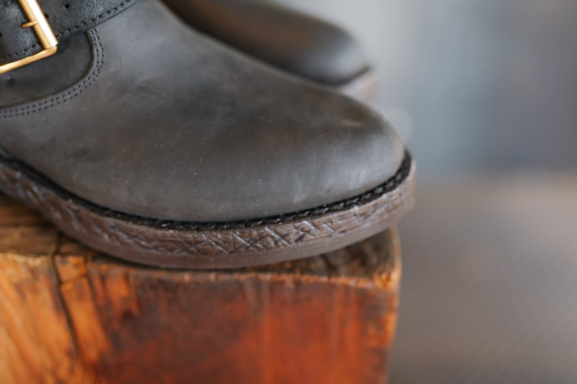 Dark leather shoes with a gold buckle on a wooden block against a blurred background