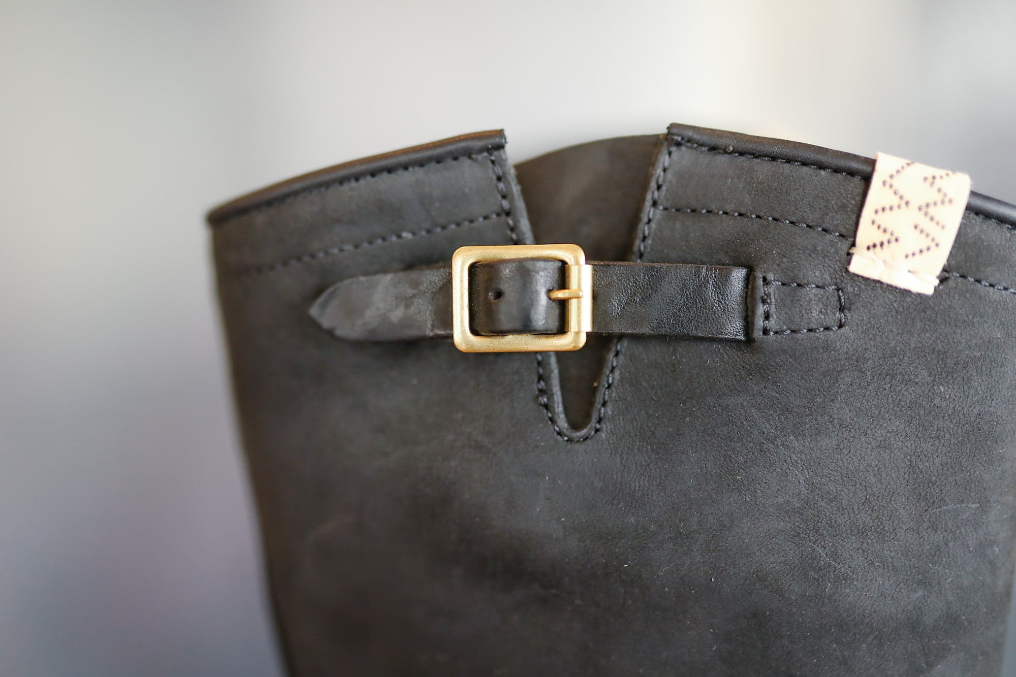 Close-up of a gray boot with a gold buckle on a light gray background