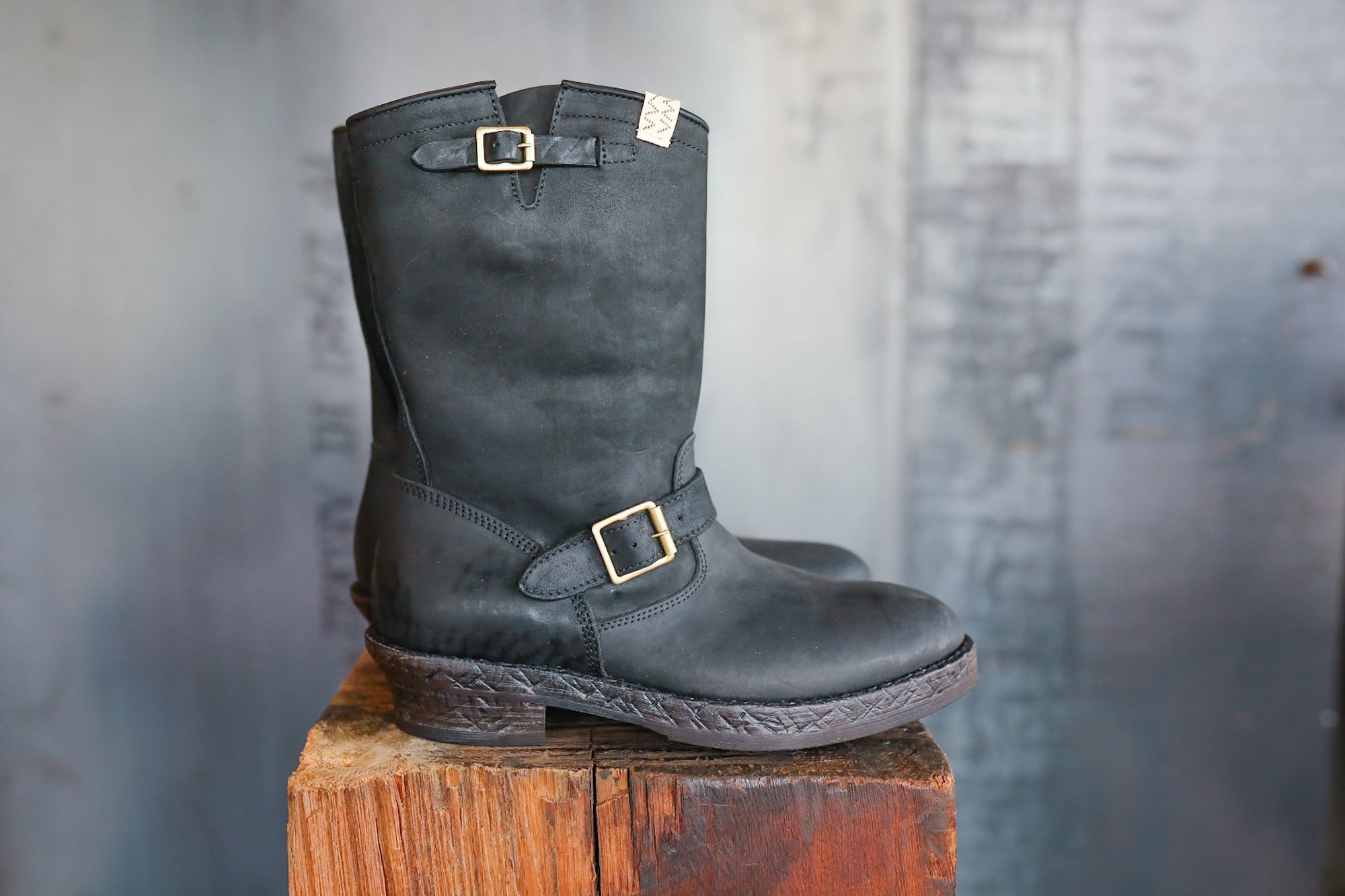Black leather boot with a buckle on a wooden block against a textured gray background