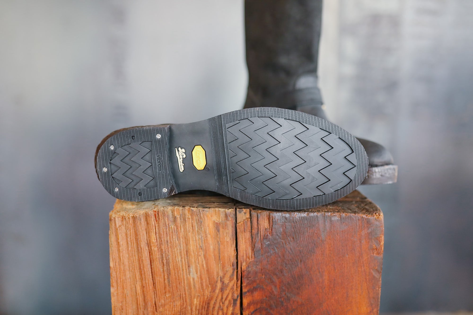 Close-up of a black boot sole with tread pattern on a wooden block, blurred background