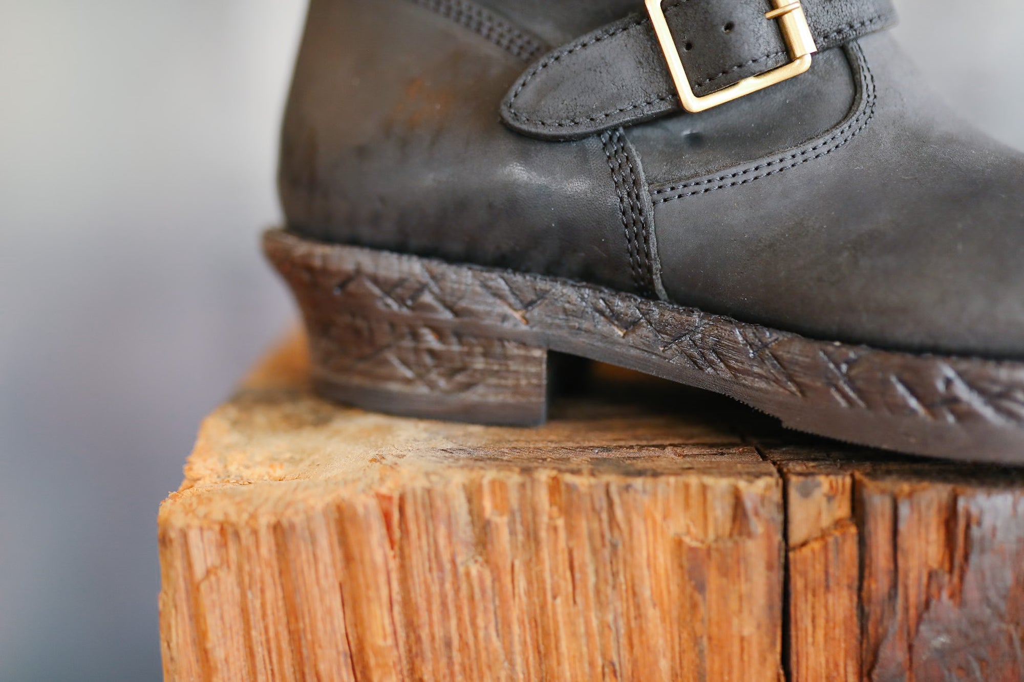 Dark leather shoe with a gold buckle on a wooden block against a neutral background