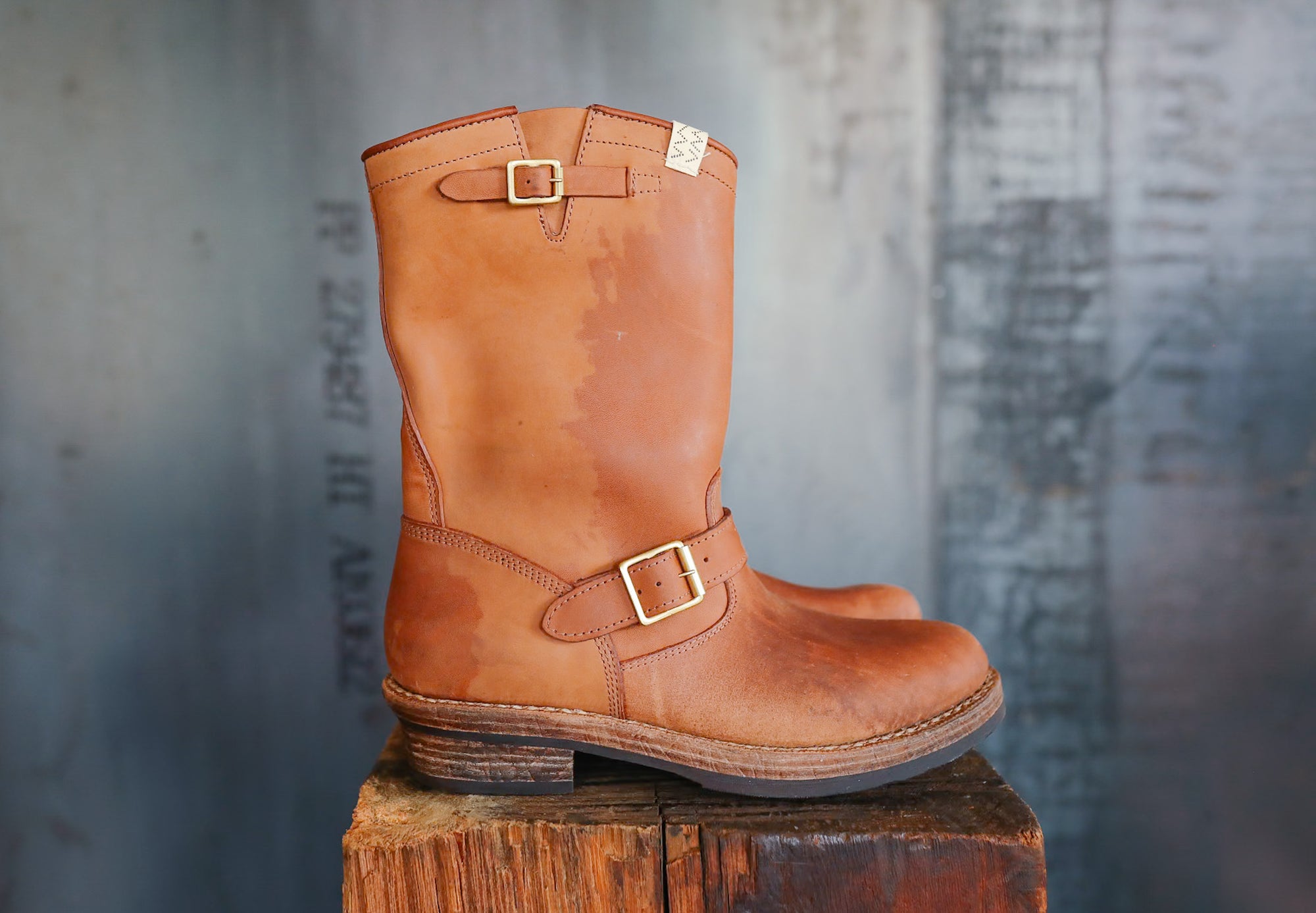 Brown leather boot with gold buckle on a wooden block against a textured gray background