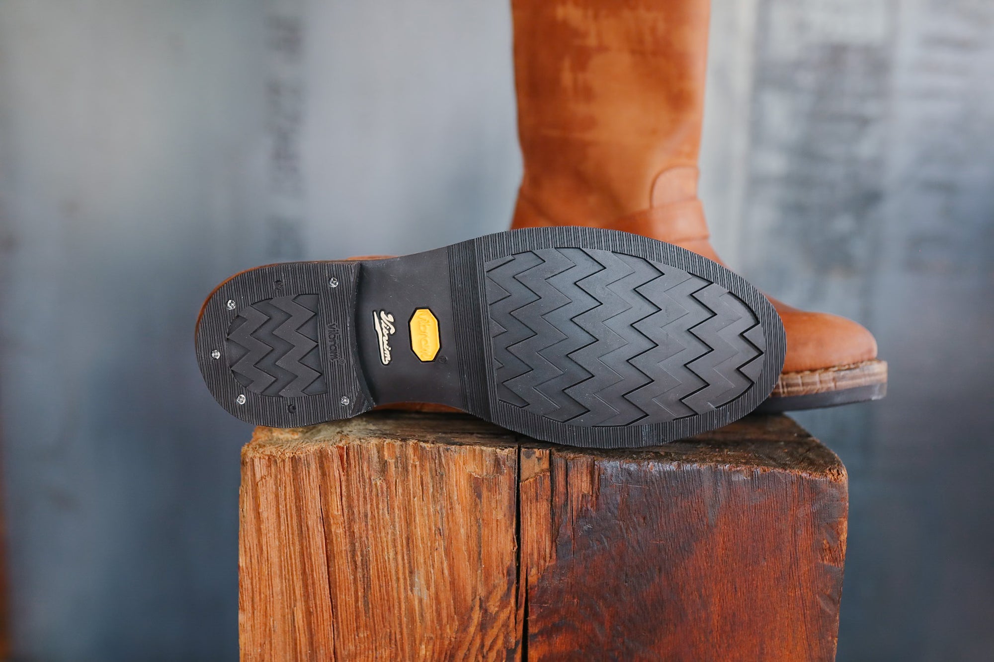 Close-up of a brown leather boot with a textured sole on a wooden block against a blurred background