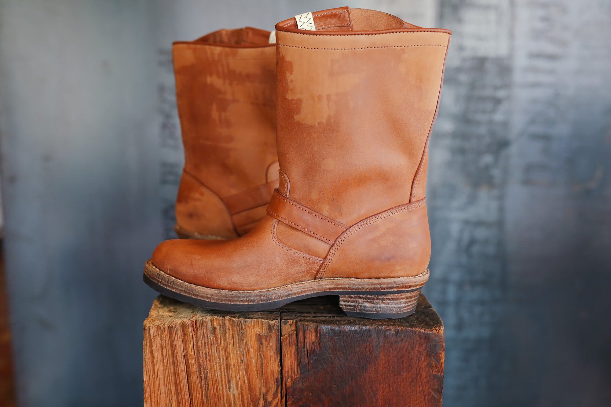 Pair of brown leather boots on a wooden block with a textured gray background