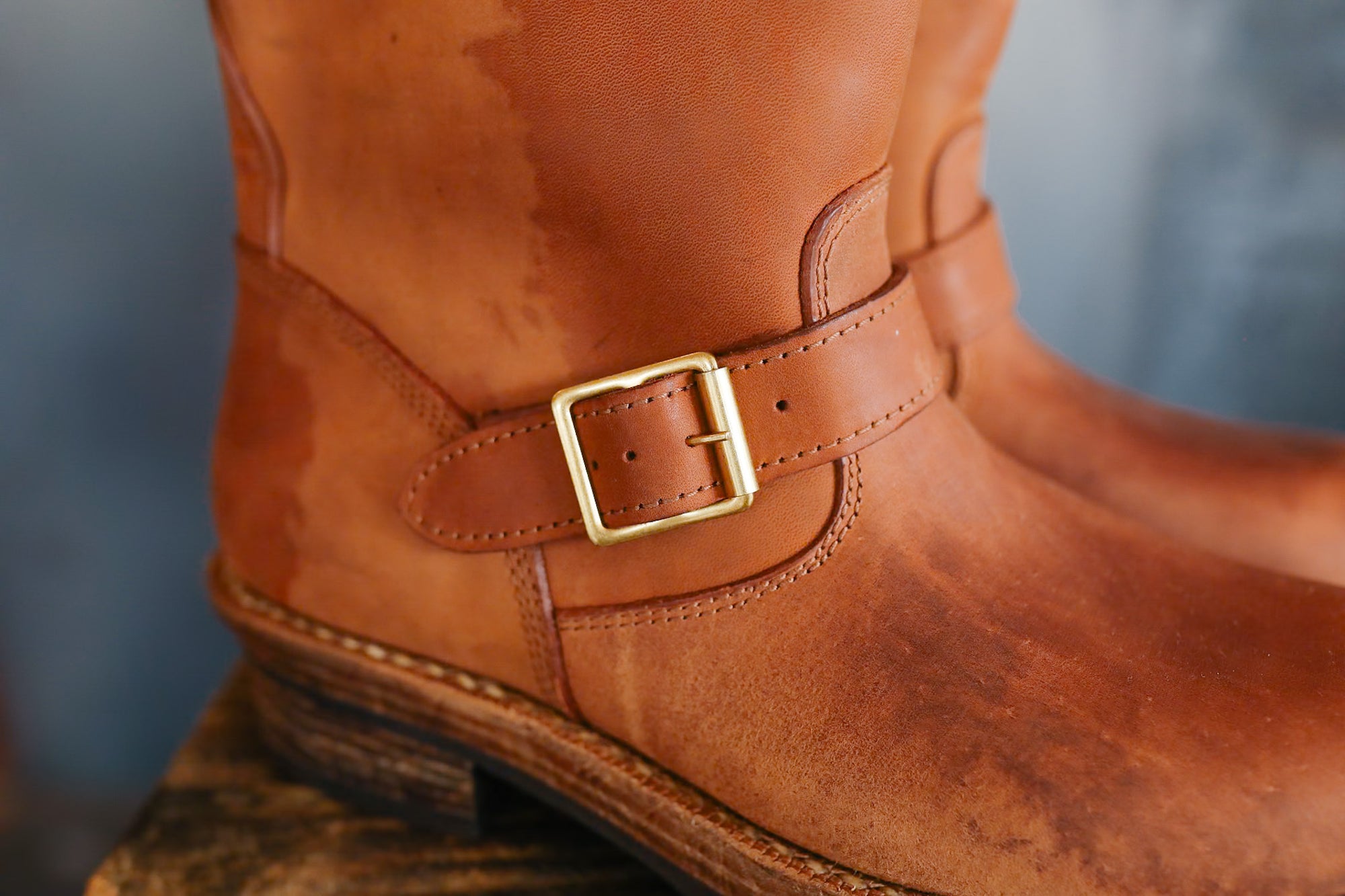 Close-up of a brown leather boot with a gold buckle on a blurred background
