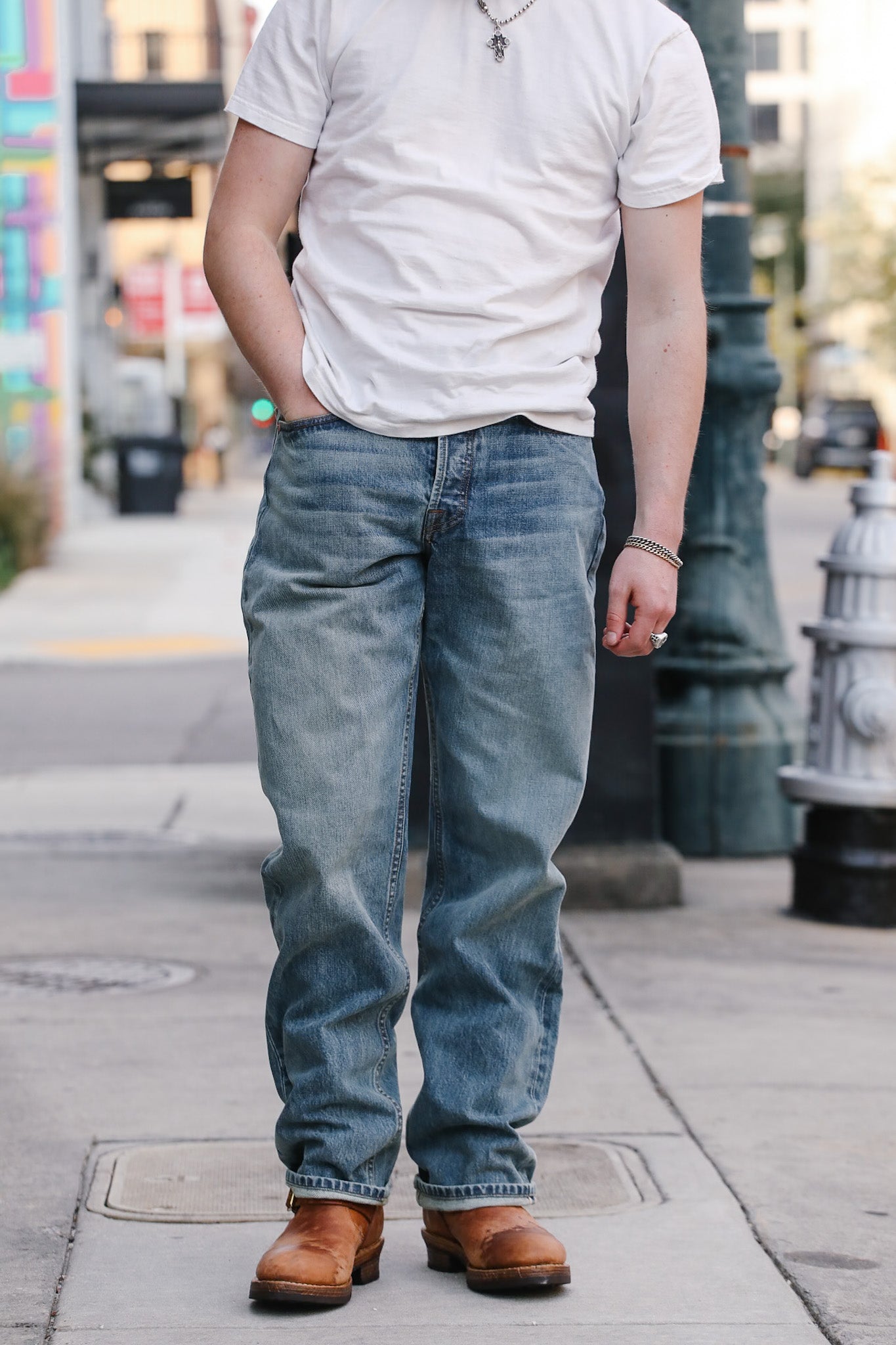 Person wearing a white t-shirt, blue jeans, and brown shoes on a city street.