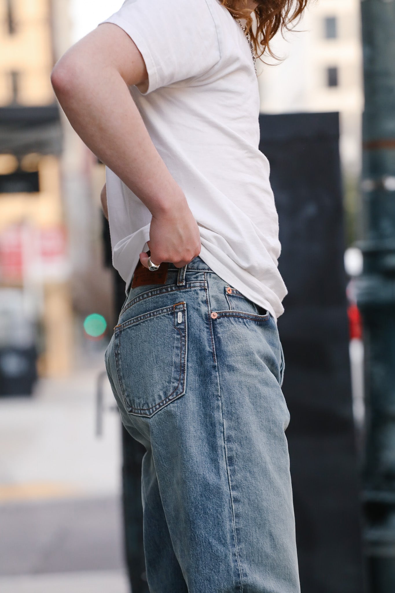 Person wearing a white t-shirt and blue jeans with a blurred urban background