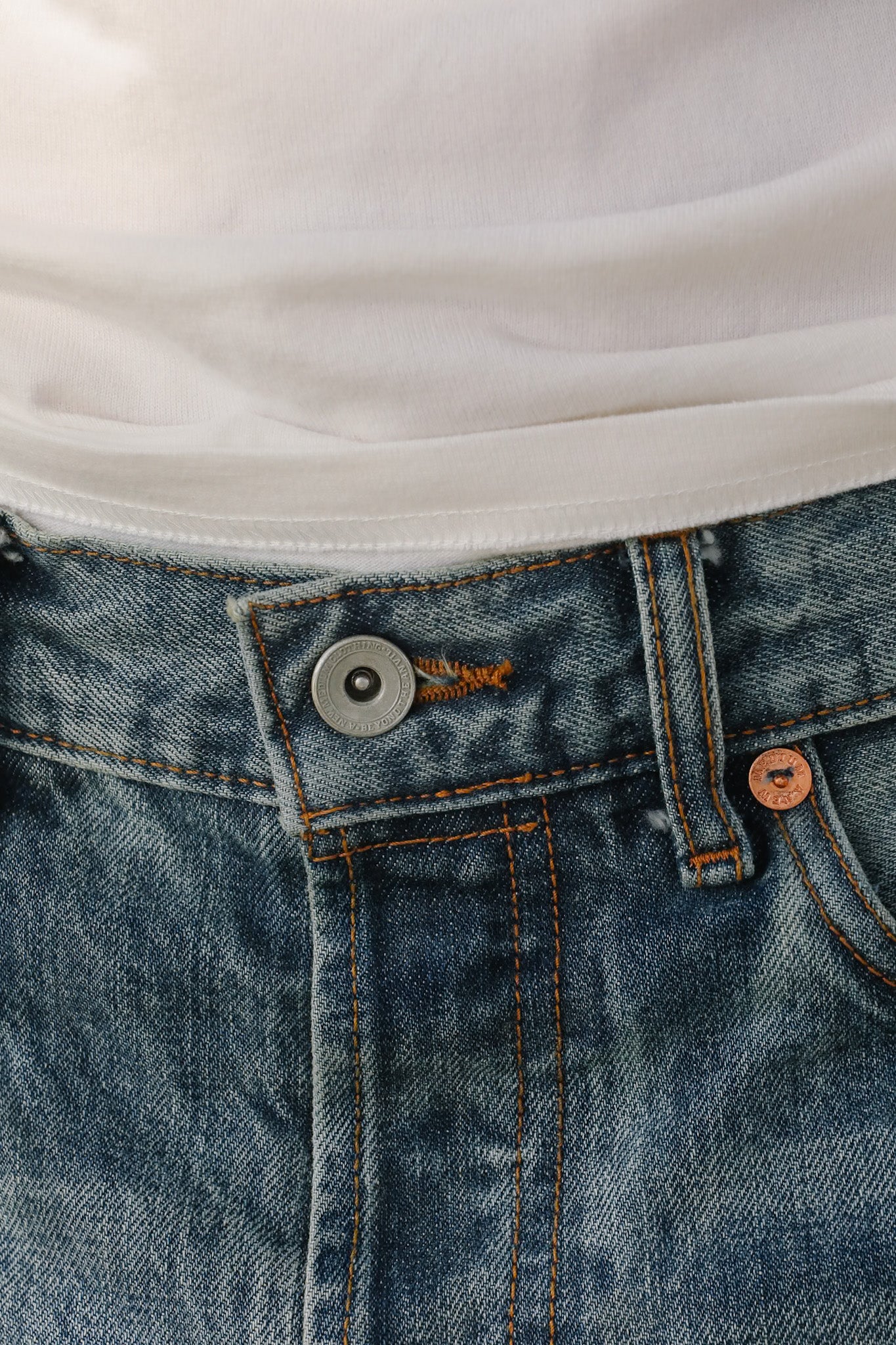 Close-up of blue jeans with a button and part of a white shirt visible