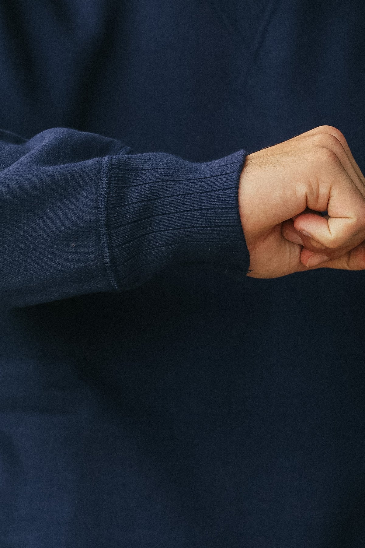 Close-up of a person's hand and wrist wearing a dark navy ribbed knit sweater sleeve.