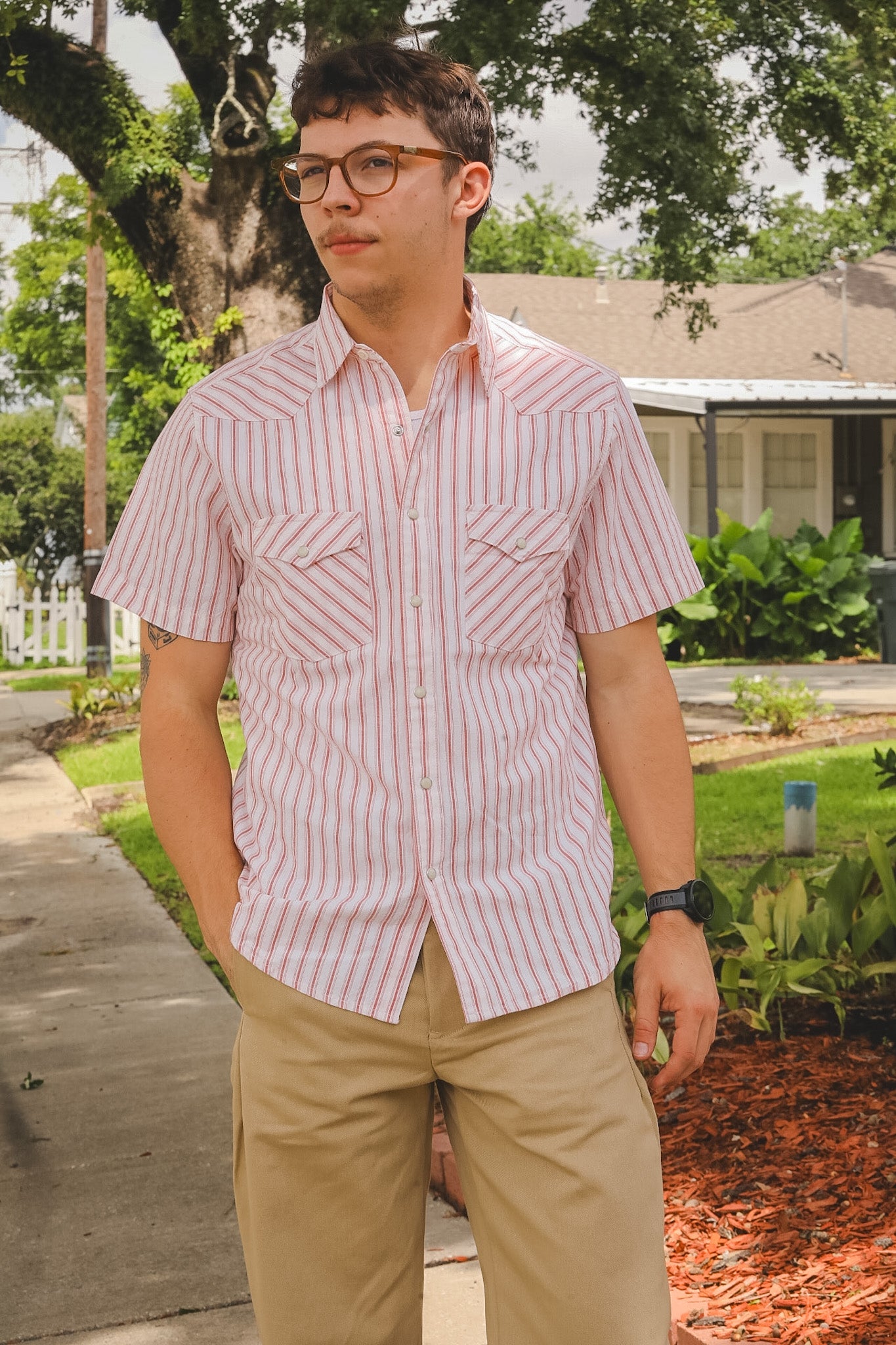 Man wearing a red and white striped shirt and beige pants standing outdoors.