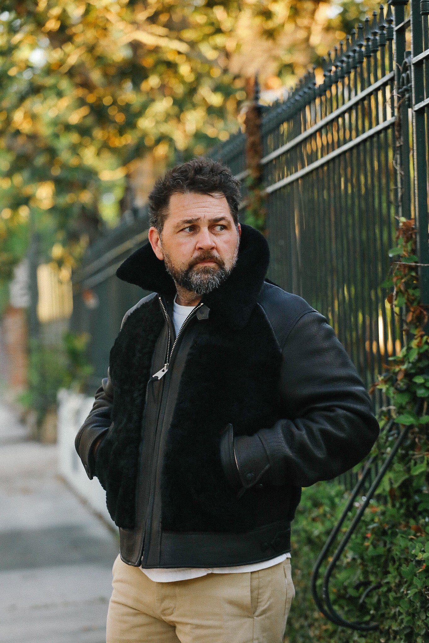Man wearing a black jacket standing outdoors with greenery in the background