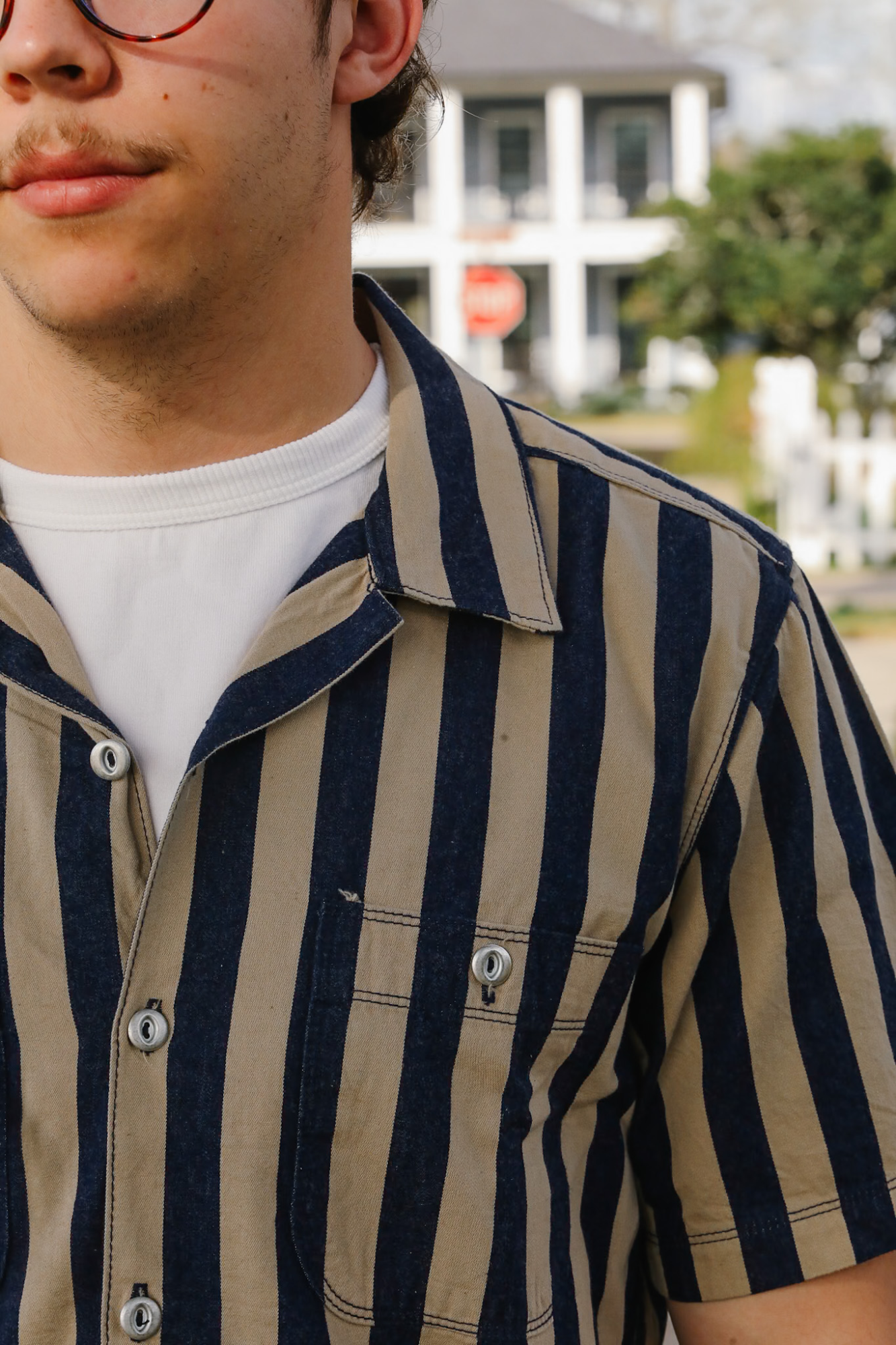 Close-up of a person wearing a navy and beige striped shirt with a blurred outdoor background.