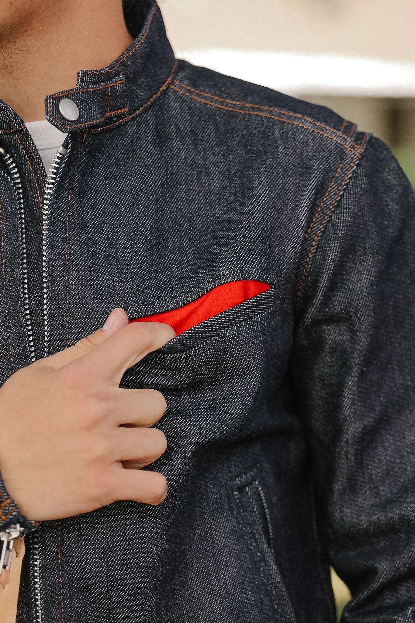 Person wearing a dark denim jacket with a red lining inside, holding the jacket open.