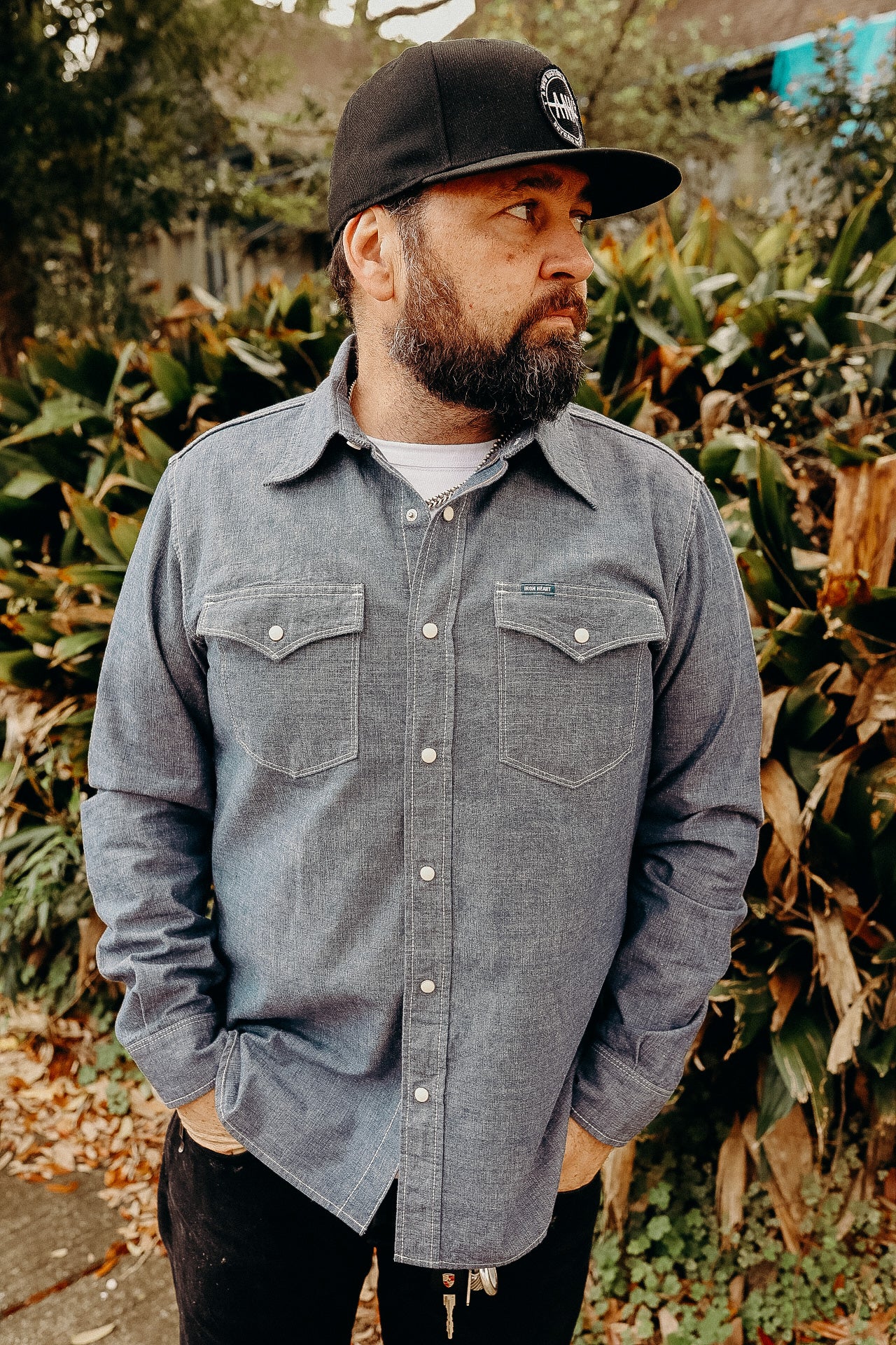 A person wearing a blue chambray western shirt with white snaps, buttoned at the collar, and two front pockets.